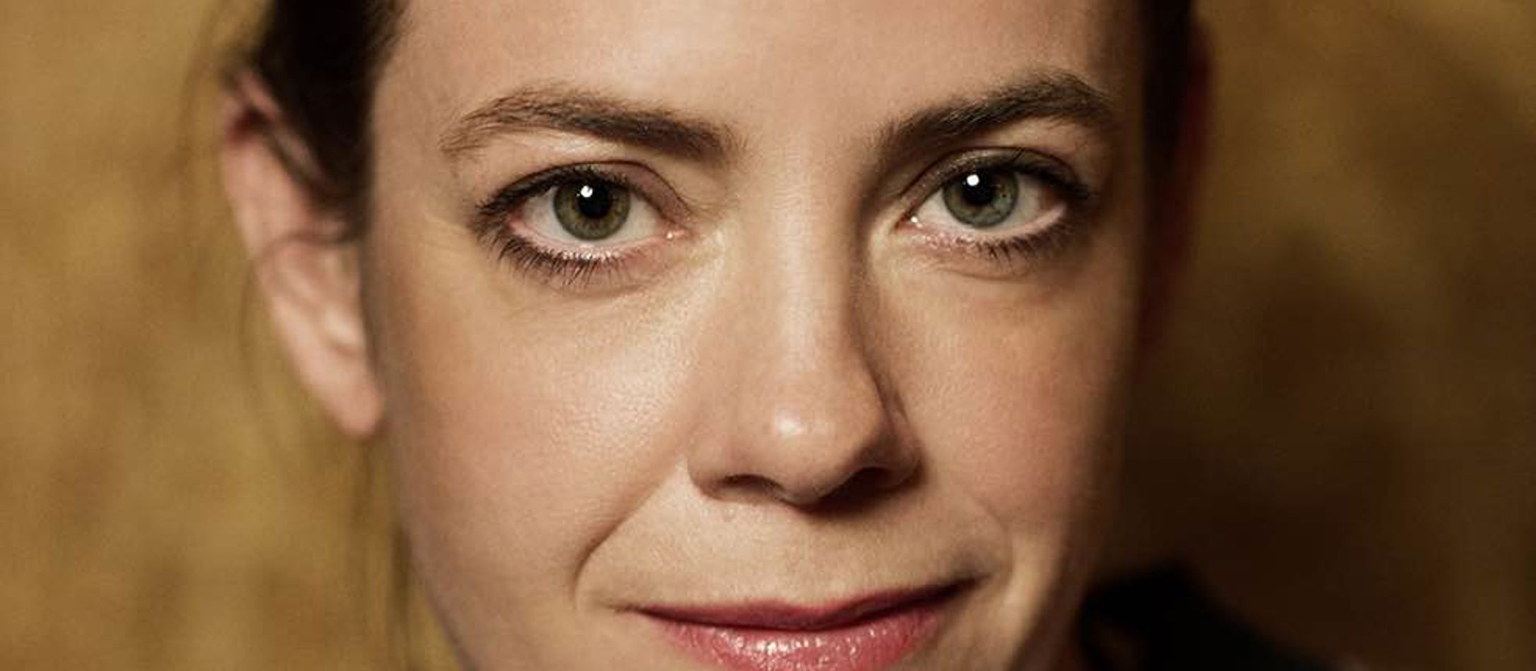 Marie Koldkjær Højlund i spraglet bluse og sort opsat hår med let rosafarvede smalle læber i lille smil