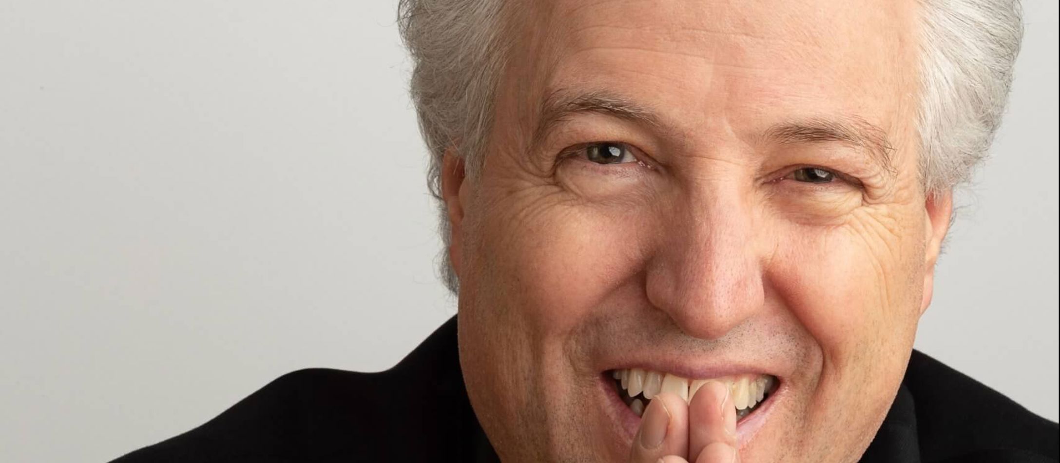Gråhårede, smilende og varme Manfred Honeck med samlede hænder foran sit smil i sort trøje.