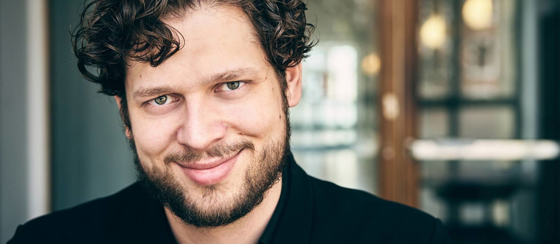 Nicolai Elsberg iført sort skjorte og kruset mørkt hår