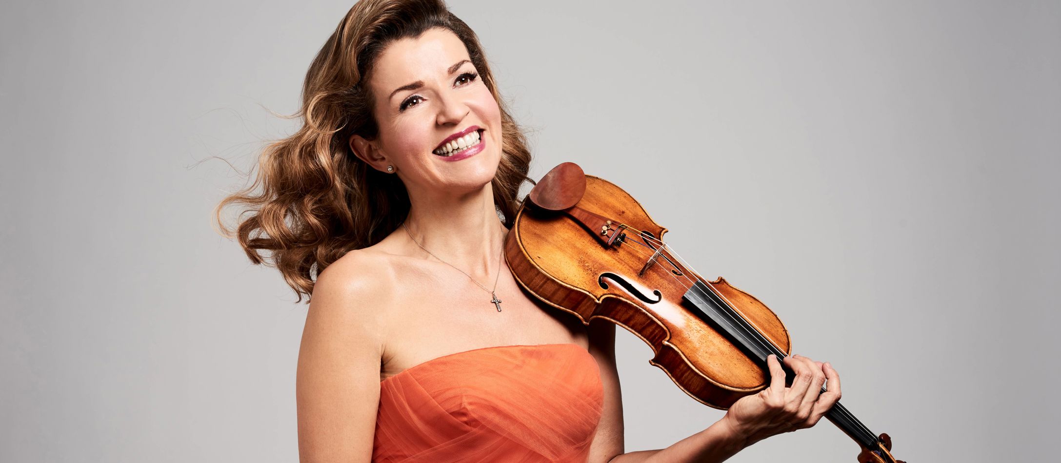 Anne-Sophie Mutter iført orange kjole med violin lagt mod skulderen