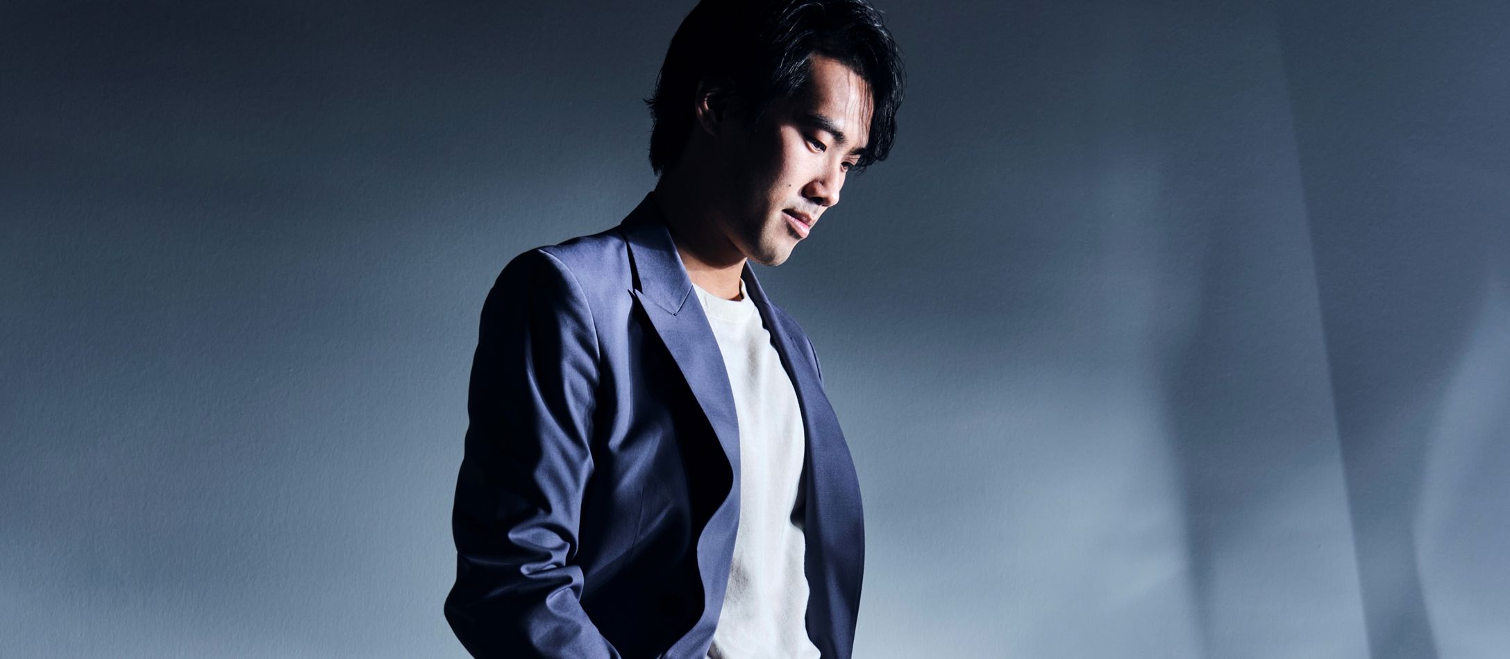 Mand med hænderne i lommen, i grå blazer foran blågrå baggrund