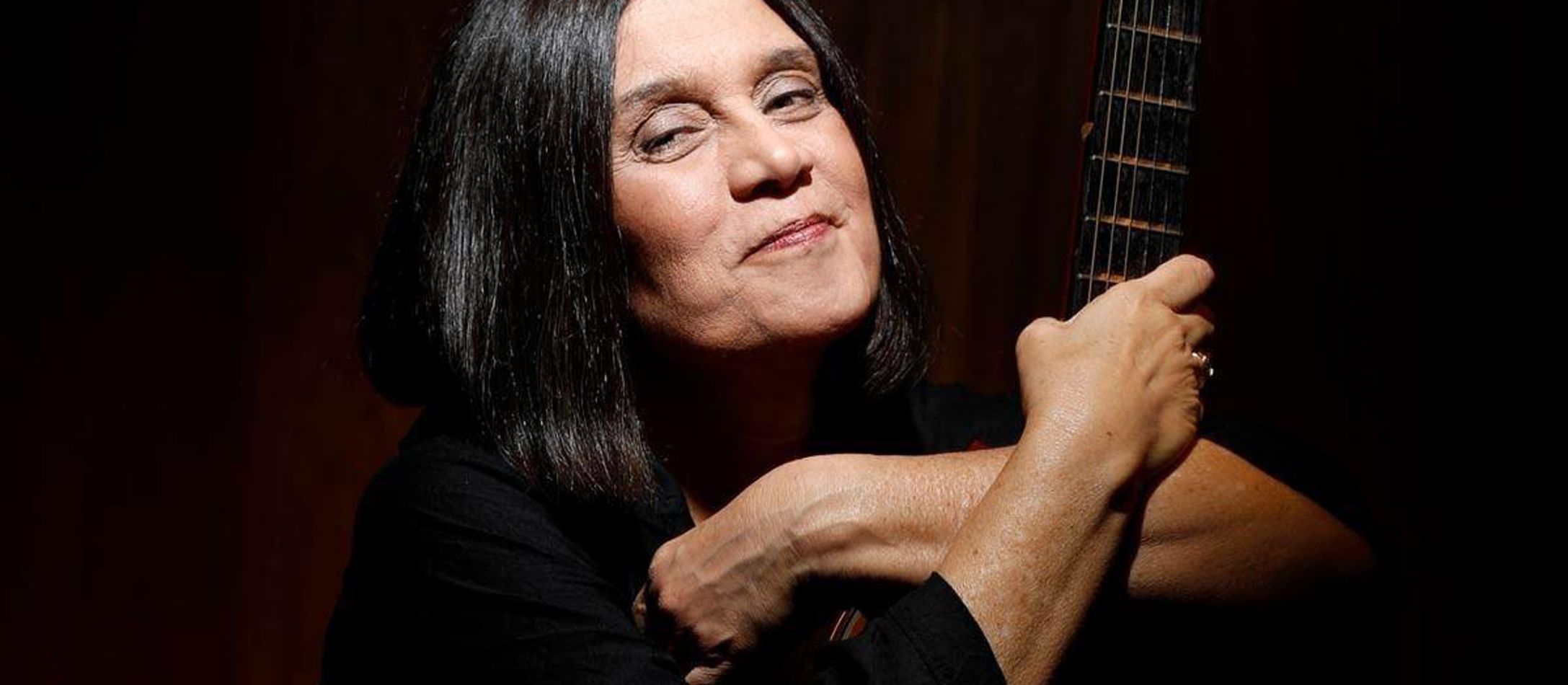 Joyce Moreno smiler let iført sort beklædning foran mørk baggrund