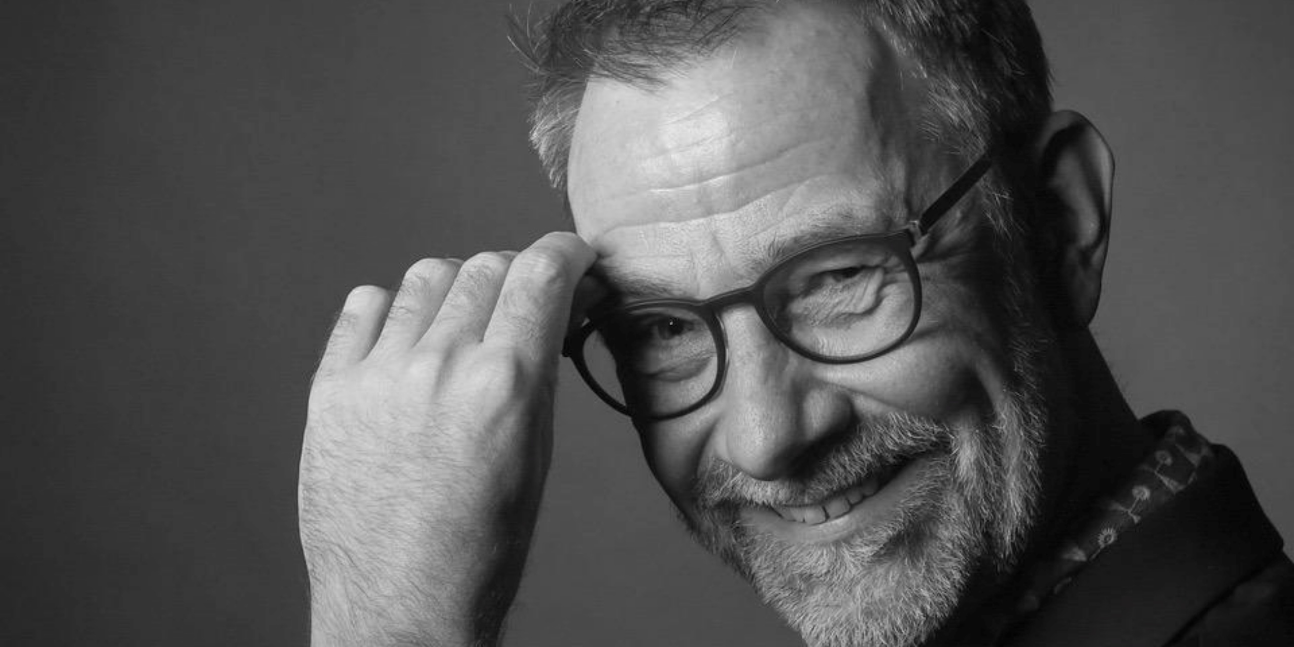 Mand med briller, kigger ind i kameraet foran en grå baggrund.