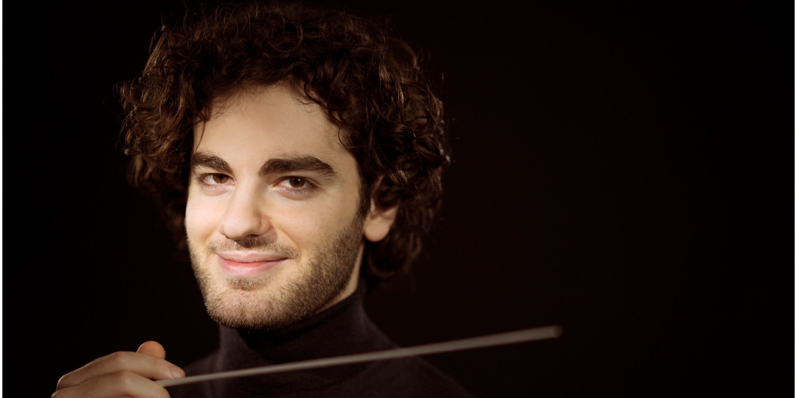 Mand med dirigentstok, smiler til kameraet.