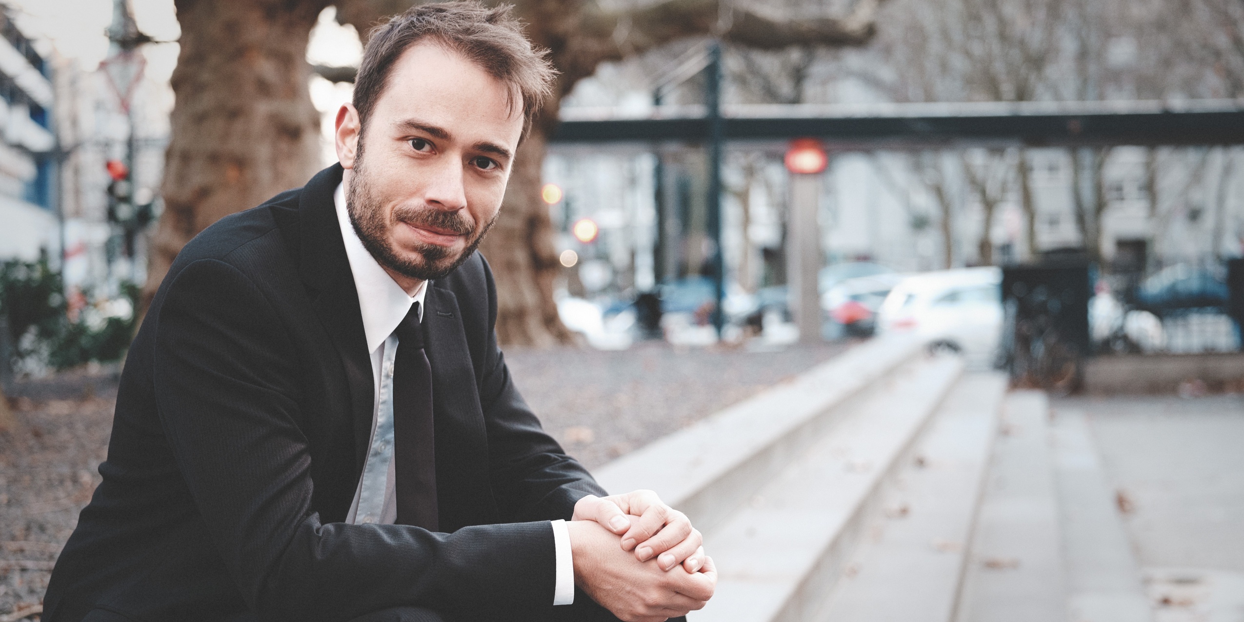 Mand sidder udenfor på trappetrin i sort blazer og sort slips.