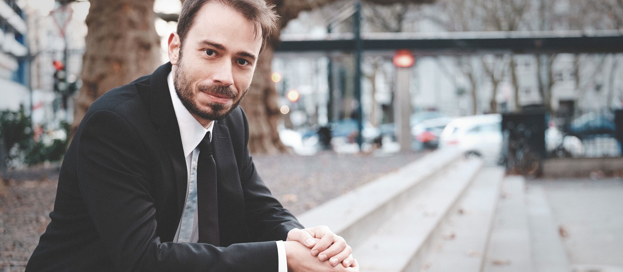 Mand sidder udenfor på trappetrin i sort blazer og sort slips.