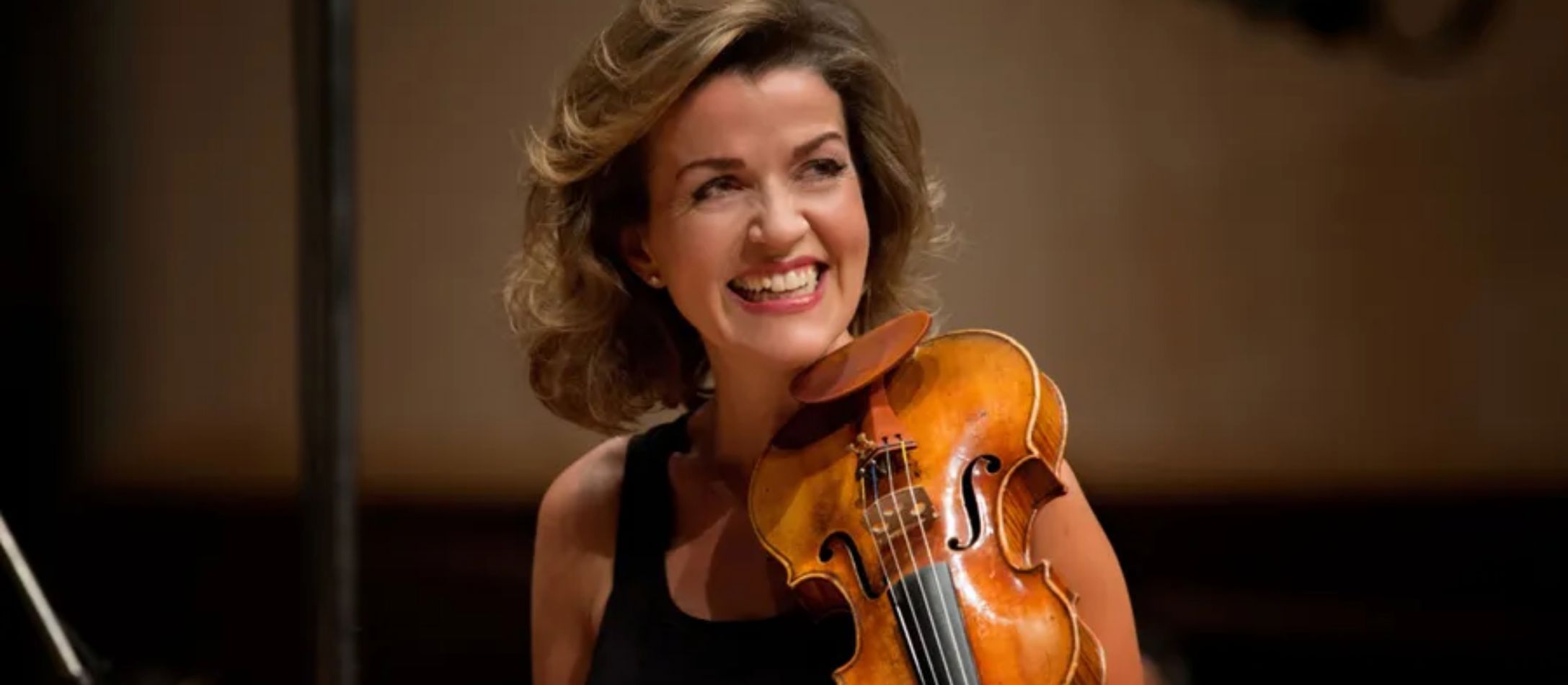 Kvinde i sort kjole, spiller smilende sin violin.