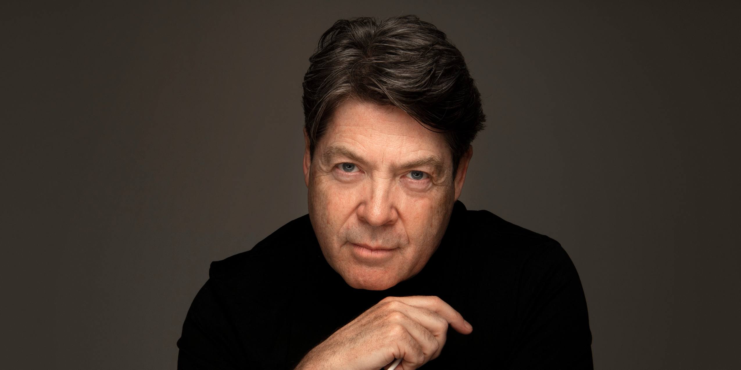 Nick Davies med mørkebrun baggrund og med dirigentpind i hånden