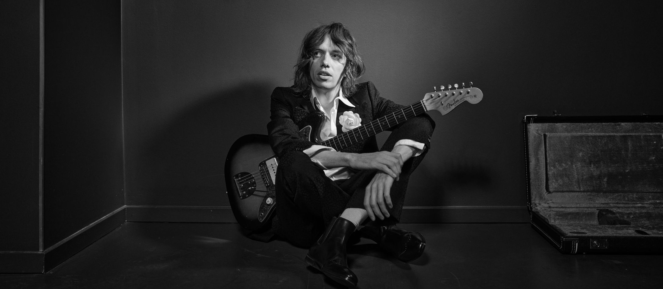 Carl Emil Petersen i sort hvid med korslagte ben og guitar i forbindelse med hans koncert i DR Koncerthus.