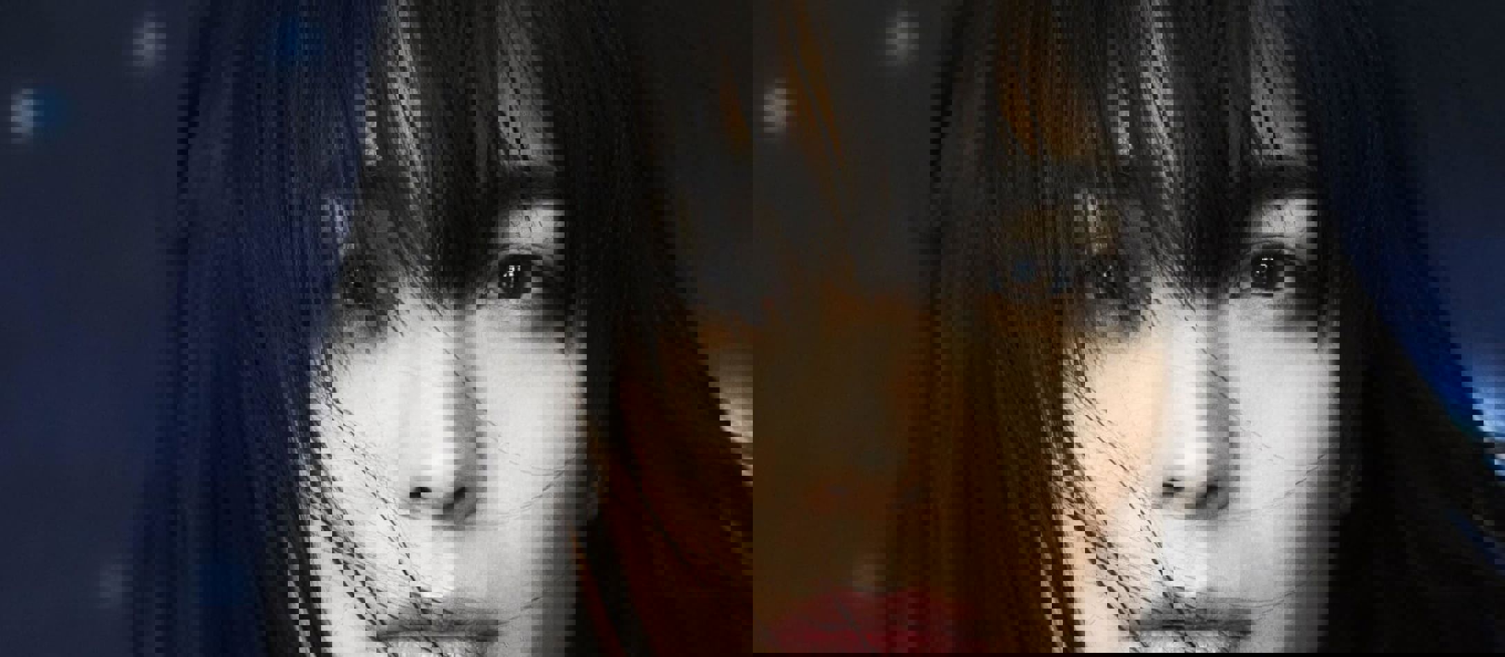 Alice Sara Ott med mørkt pandehår, der falder foran dybe, brune øjne med bare skuldre og høj hals på bluse med blå baggrund