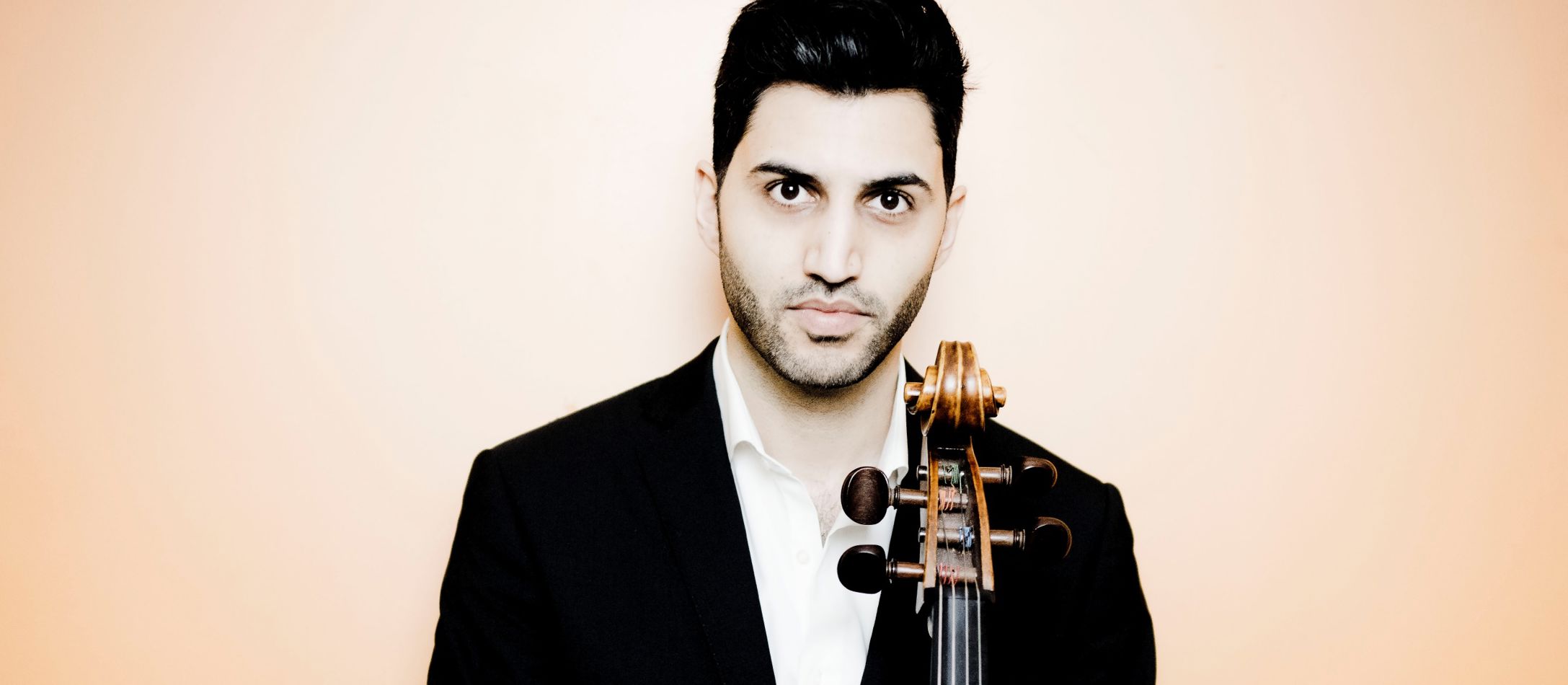 Mand med sort blazer, står med sin cello og kigger ind i kameraet.