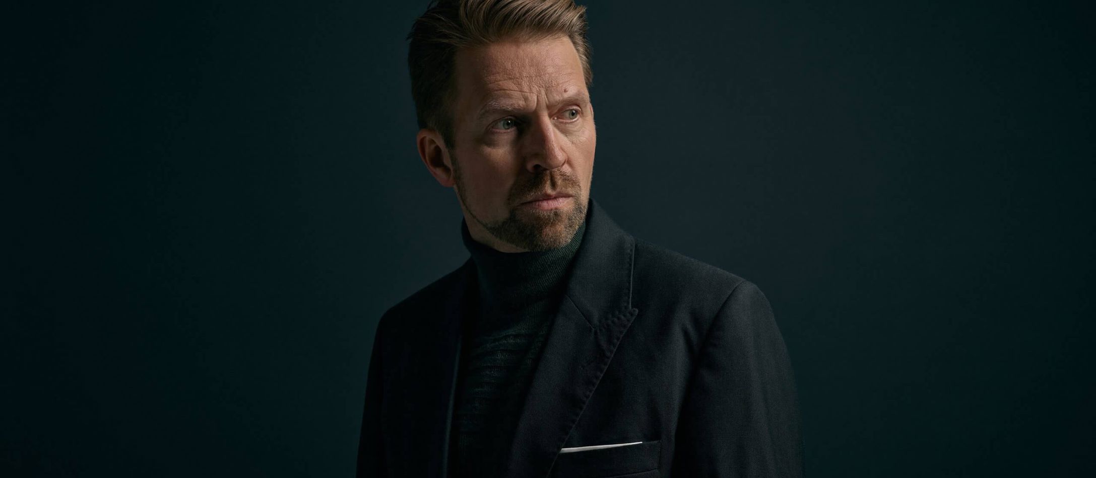 Alvorlige Leif Ove Andsnes iført helt sort jakkesæt kigger mod sin venstre på sort baggrund.
