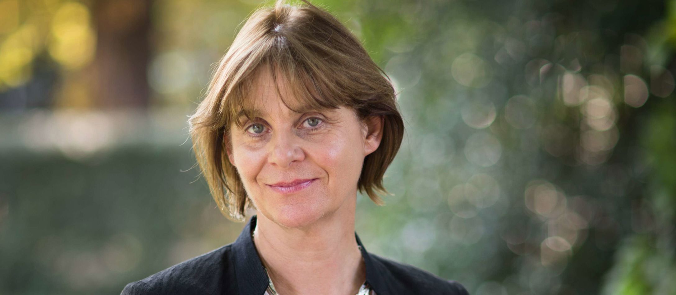 Verdenskendt gerontolog Sarah Harper med mørk kort hår og fin sølvhalskæde fotograferet foran stille grønt område