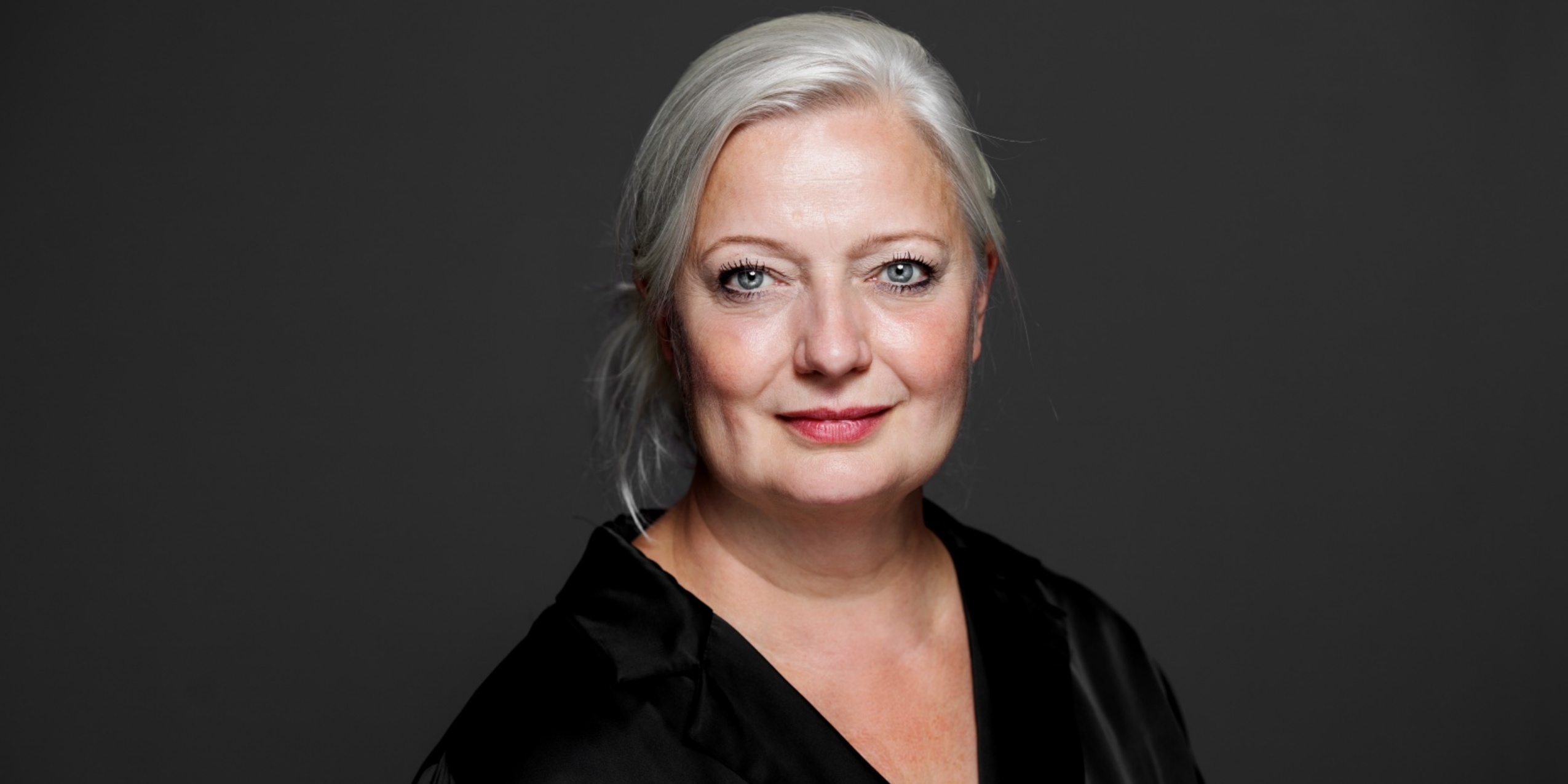 Kvinde i sort der kigger ind i kameraet foran en mørkegrå væg