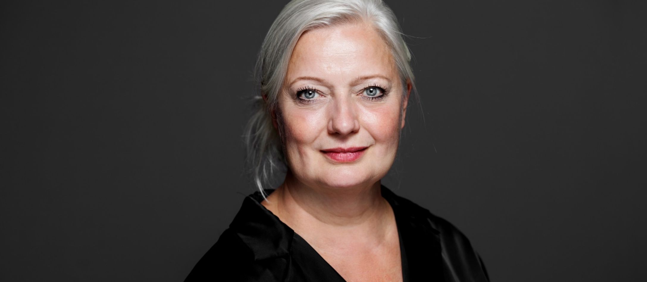Kvinde i sort der kigger ind i kameraet foran en mørkegrå væg