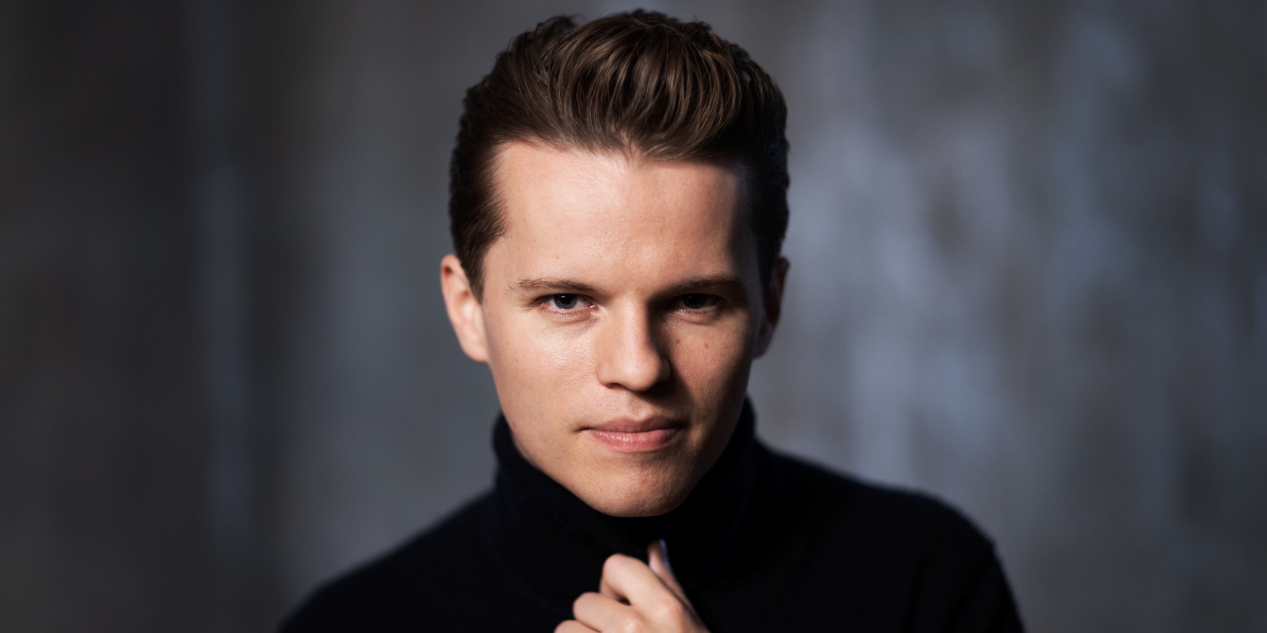 Mand i sort, kigger ind i kameraet foran mørkegrå baggrund.