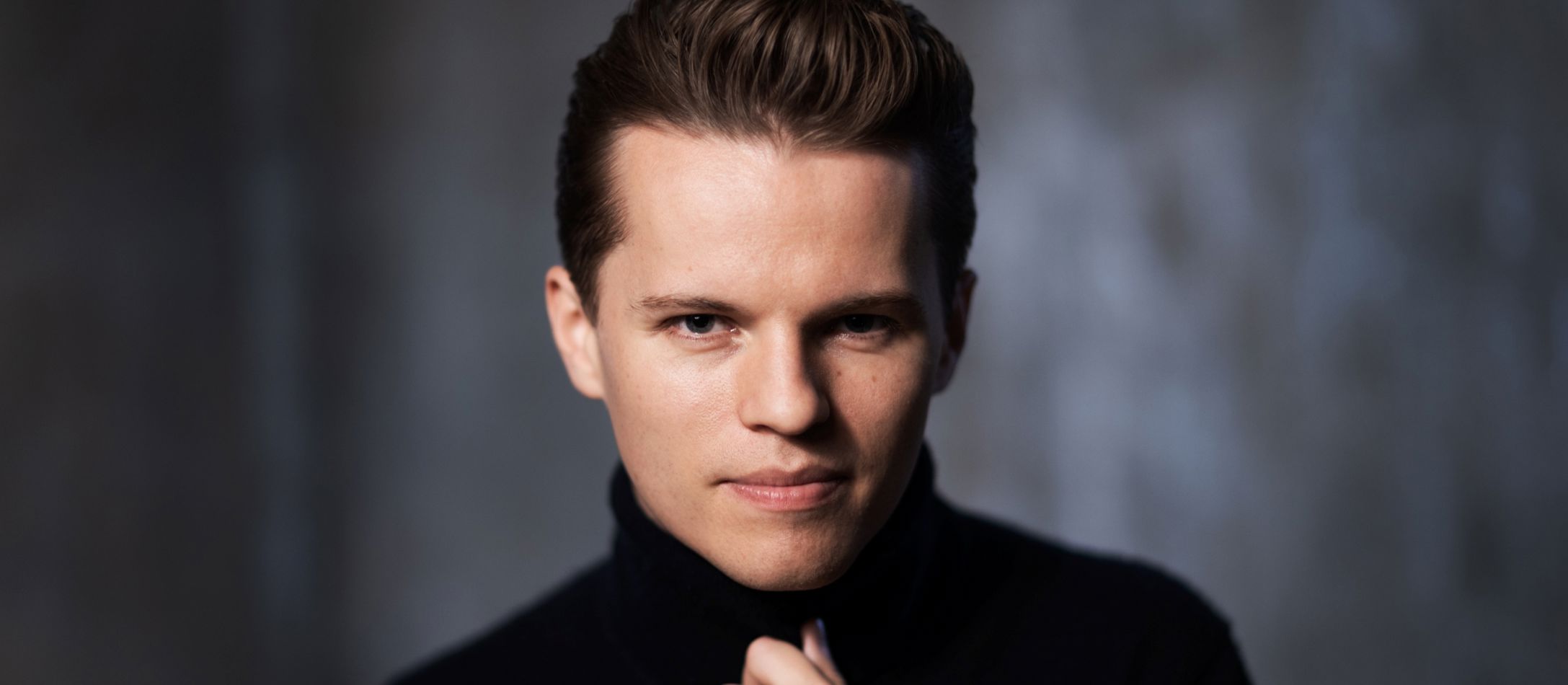 Mand i sort, kigger ind i kameraet foran mørkegrå baggrund.