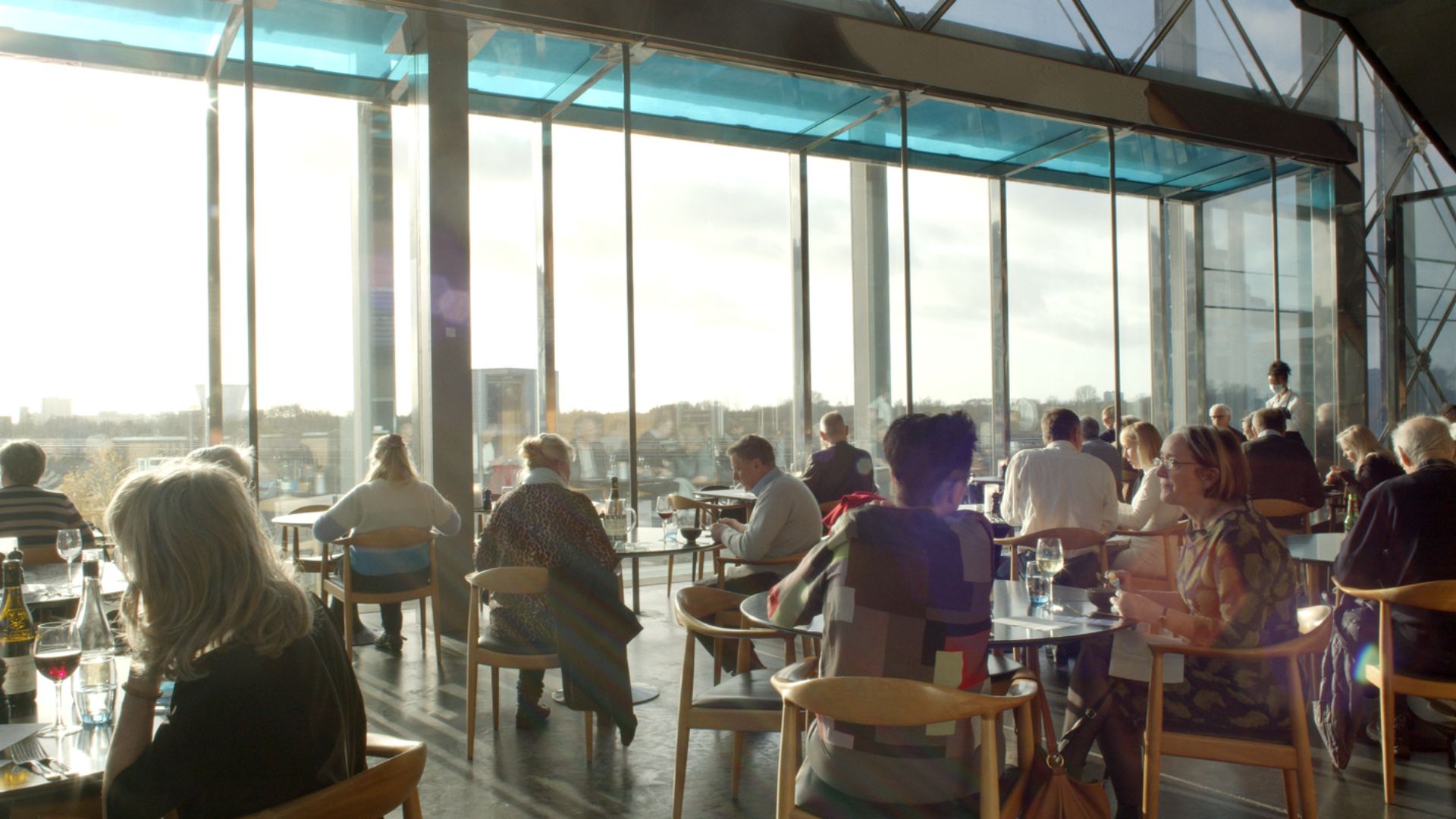 Mennesker i restauranten i DR Koncerthuset med fyldte glas kigger ud gennem viduesruderne. 