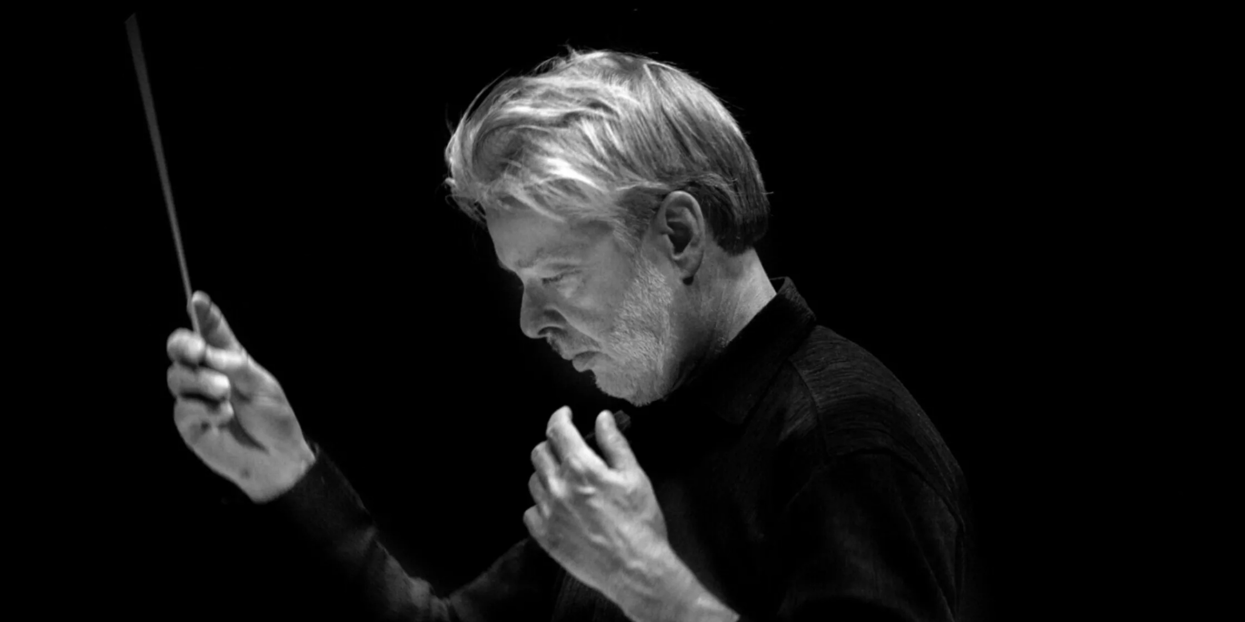 Mand i sort med en løftet dirigentstok foran sort baggrund