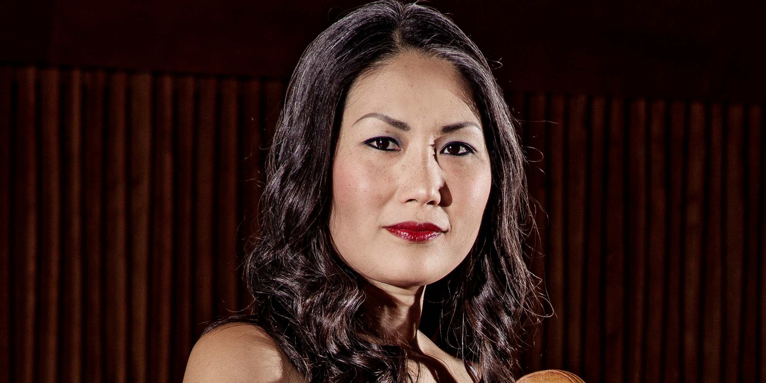 Kvinde med cello foran mørk orange bølget vægtæppe