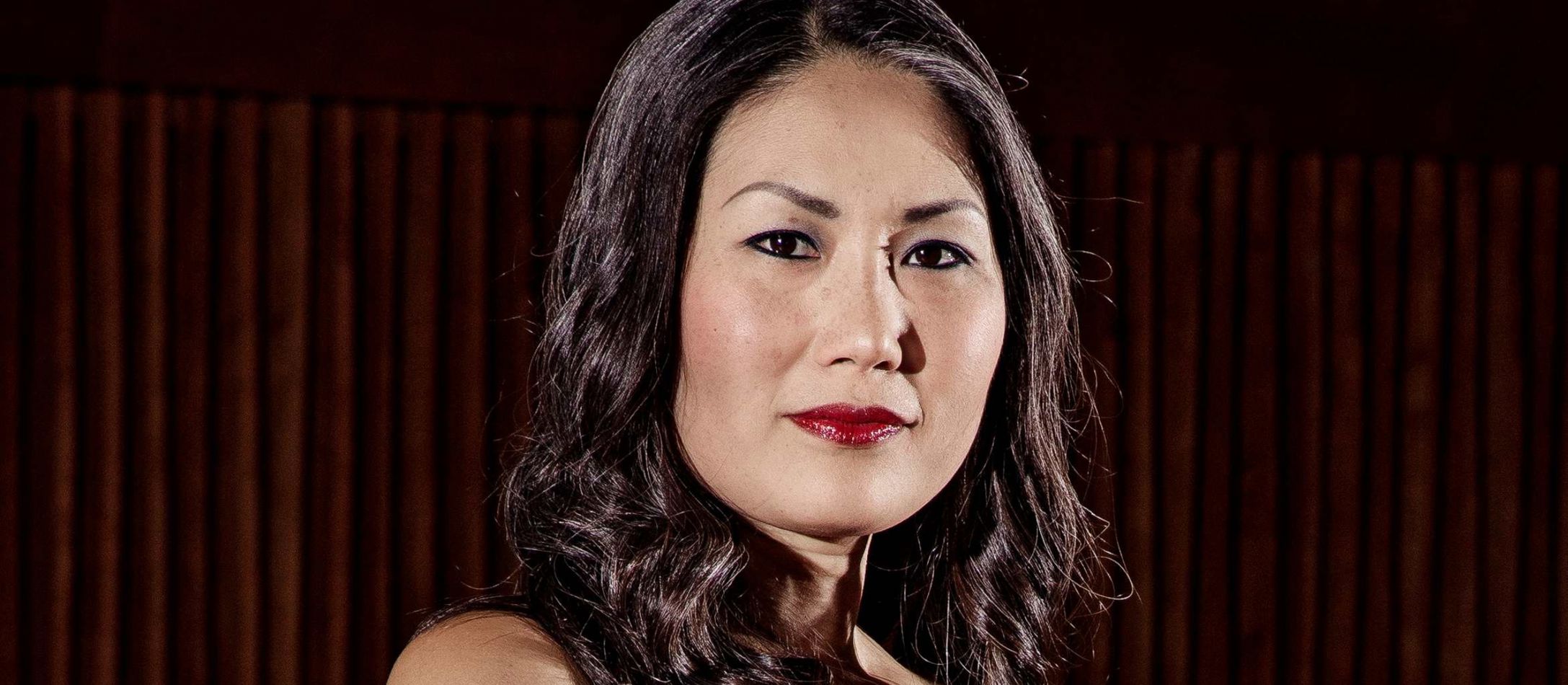 Kvinde med cello foran mørk orange bølget vægtæppe