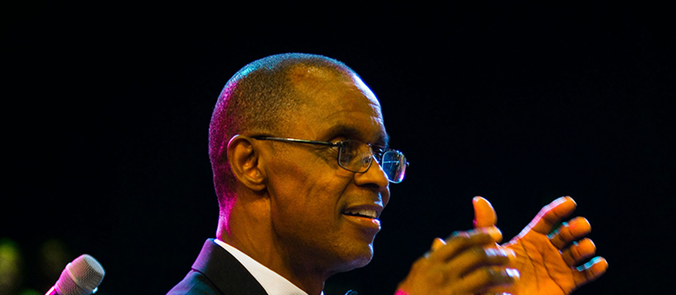 Dirigenten Charlie Young med briller og løftede hænder svagt oplyst af farver iført klassisk jakkesæt