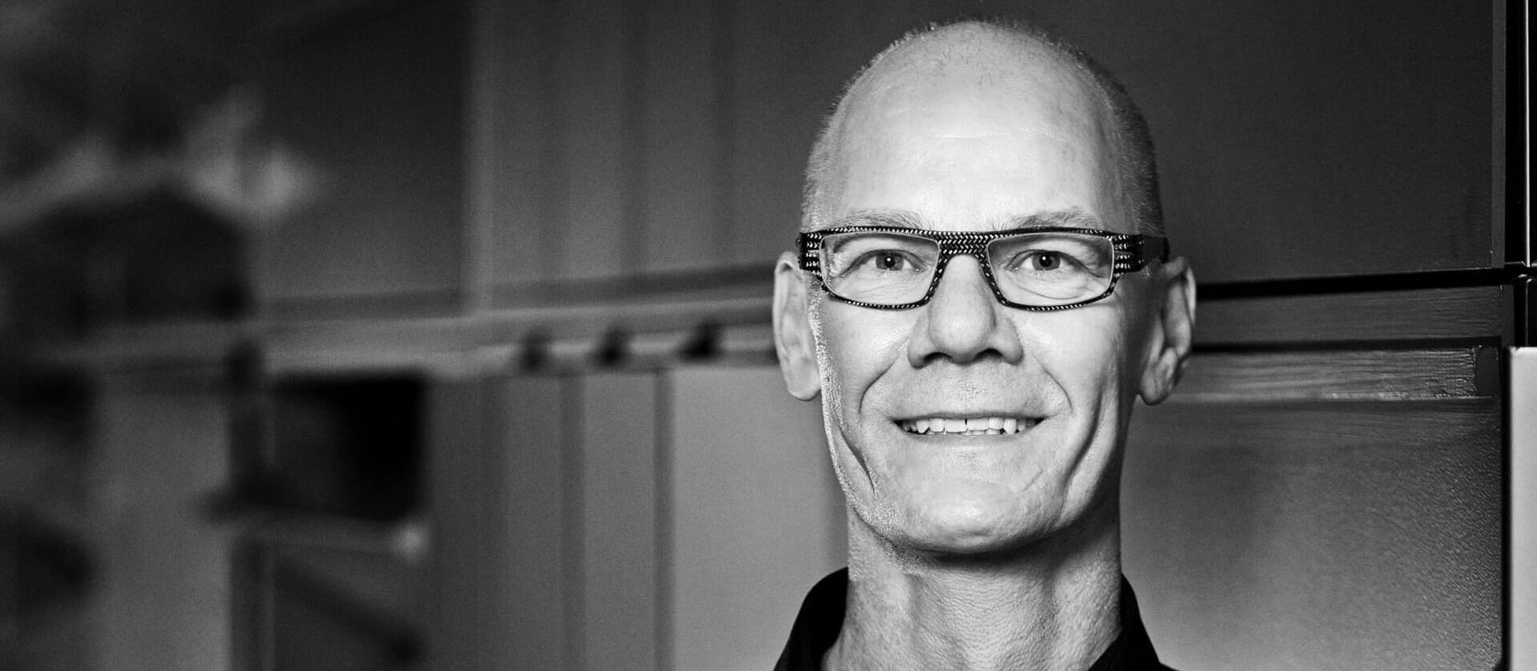 Poul Emborg med briller storsmiler iført sort skjorte.