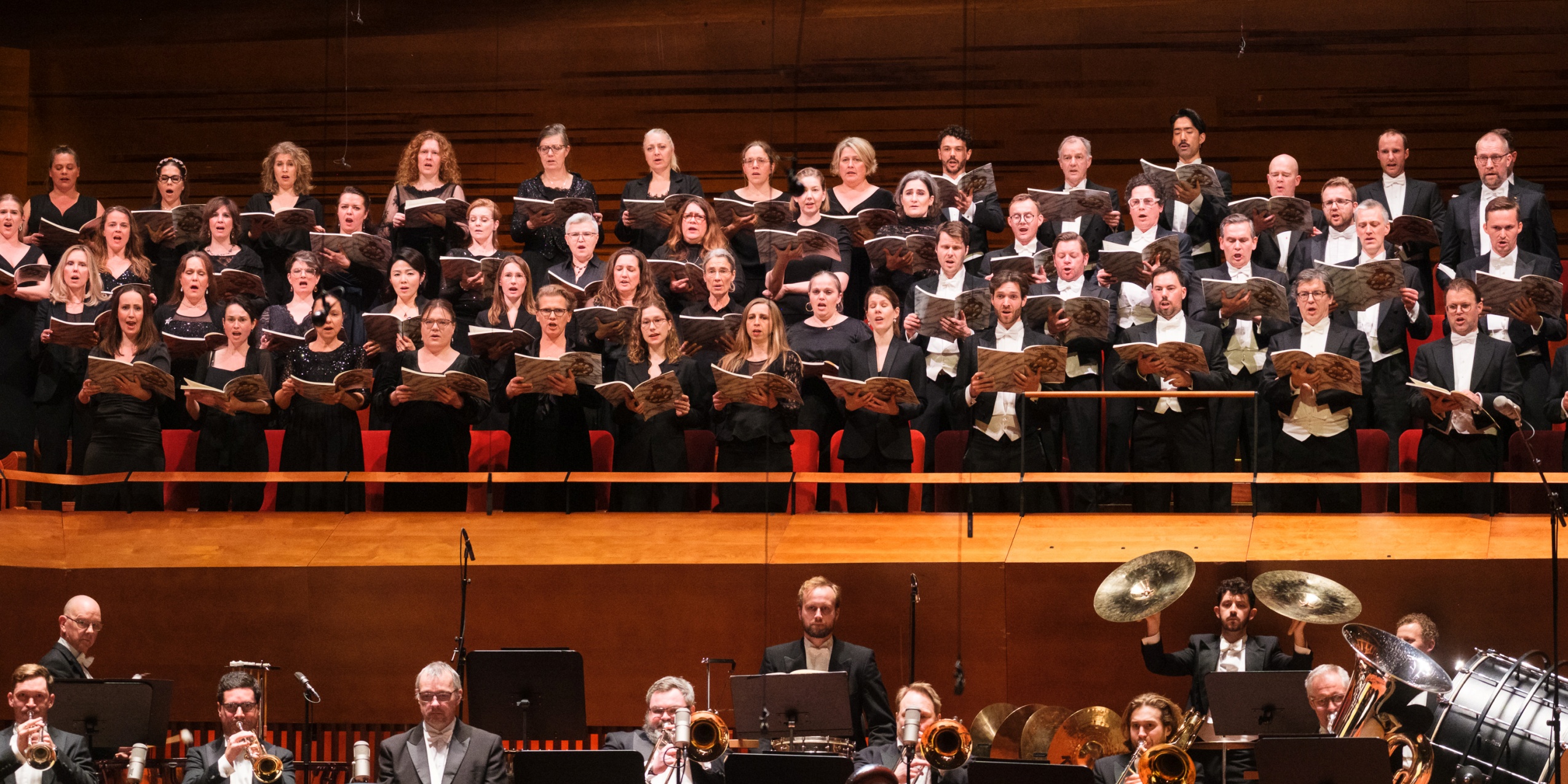 Kor der synger i koncertsalen med orkesteret i forgrunden.