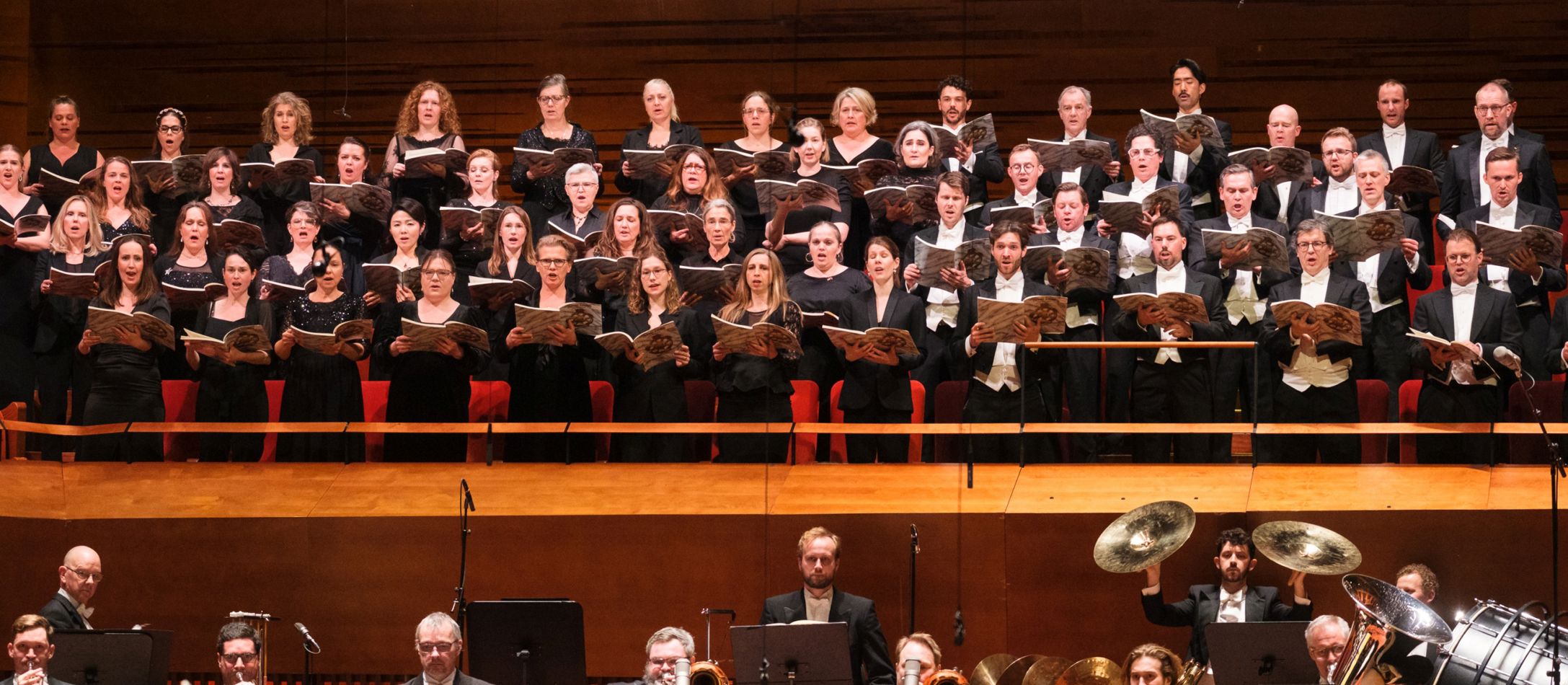 Kor der synger i koncertsalen med orkesteret i forgrunden.