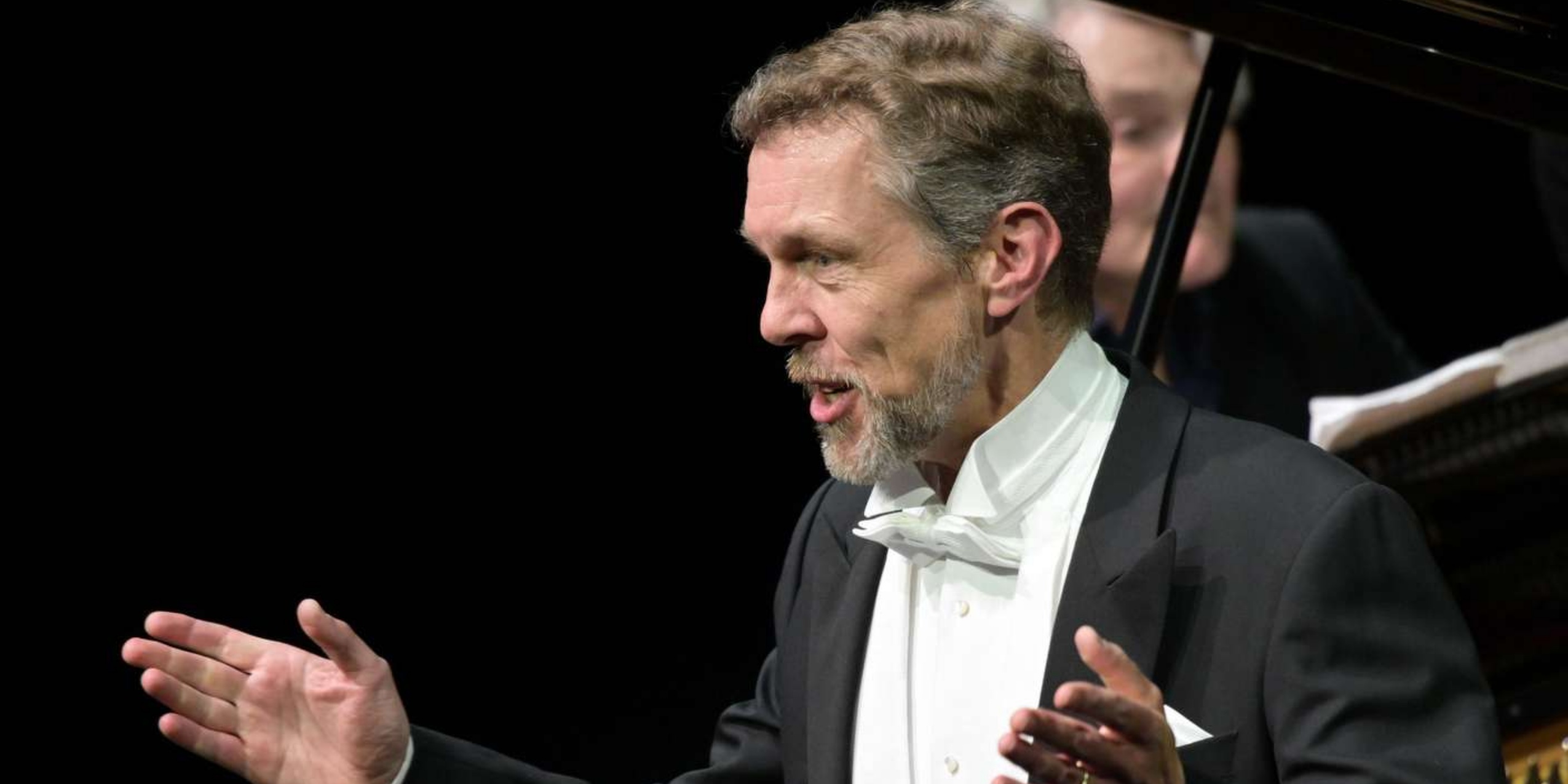 Mand i kjole og hvidt der synger foran et klaver