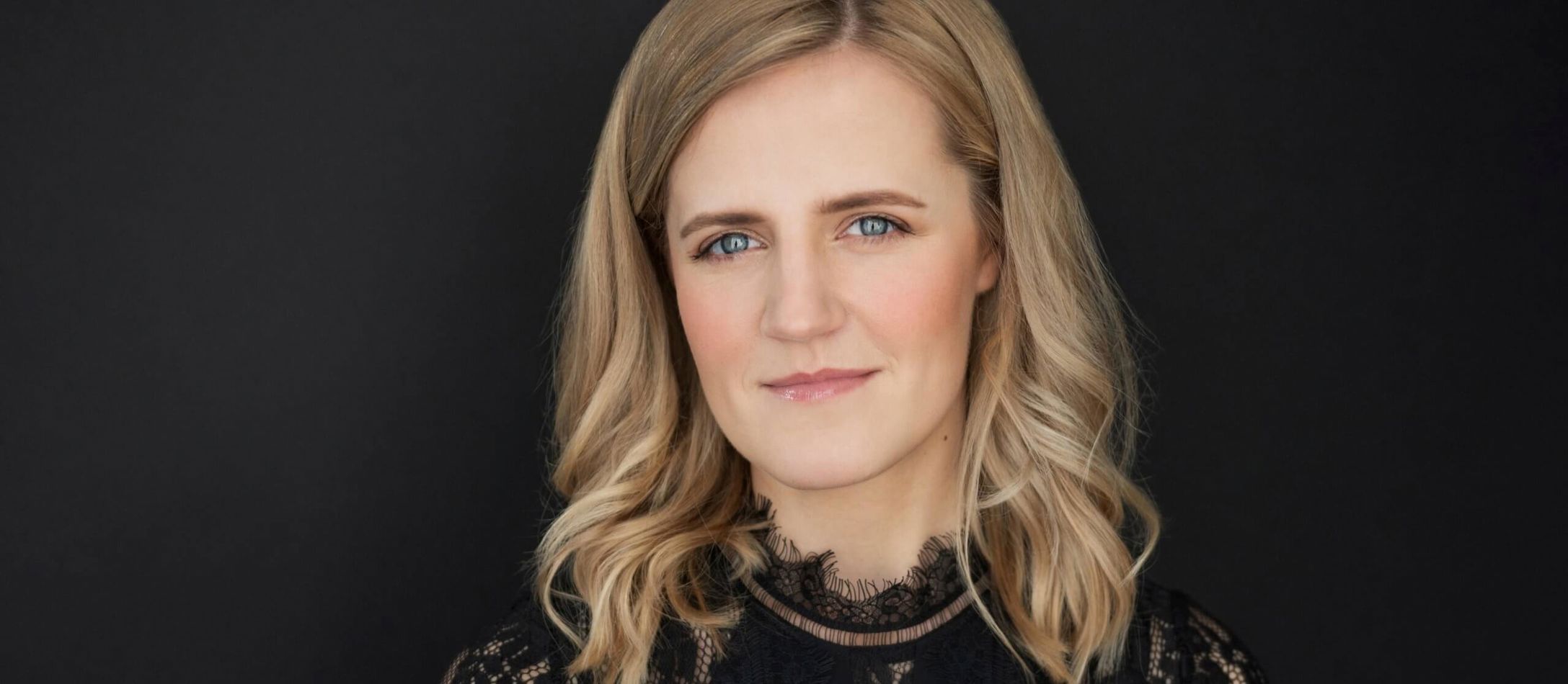 Krista Audere med blå øjne og smuk bølget lyst hår og sort blonde bluse.