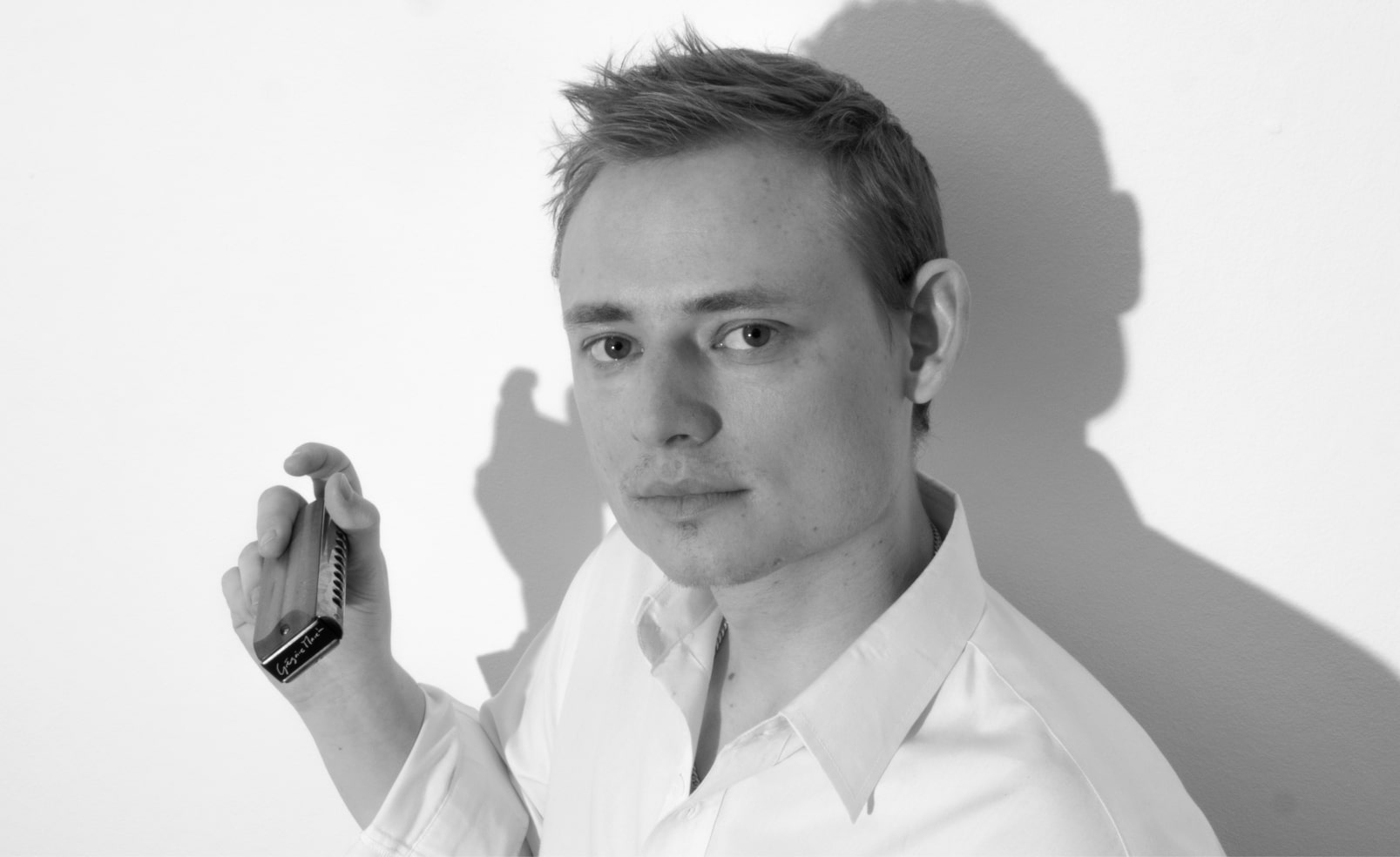 Mathias Heise med harmonika i højre hånd iført hvid skjorte foran hvid baggrund. 