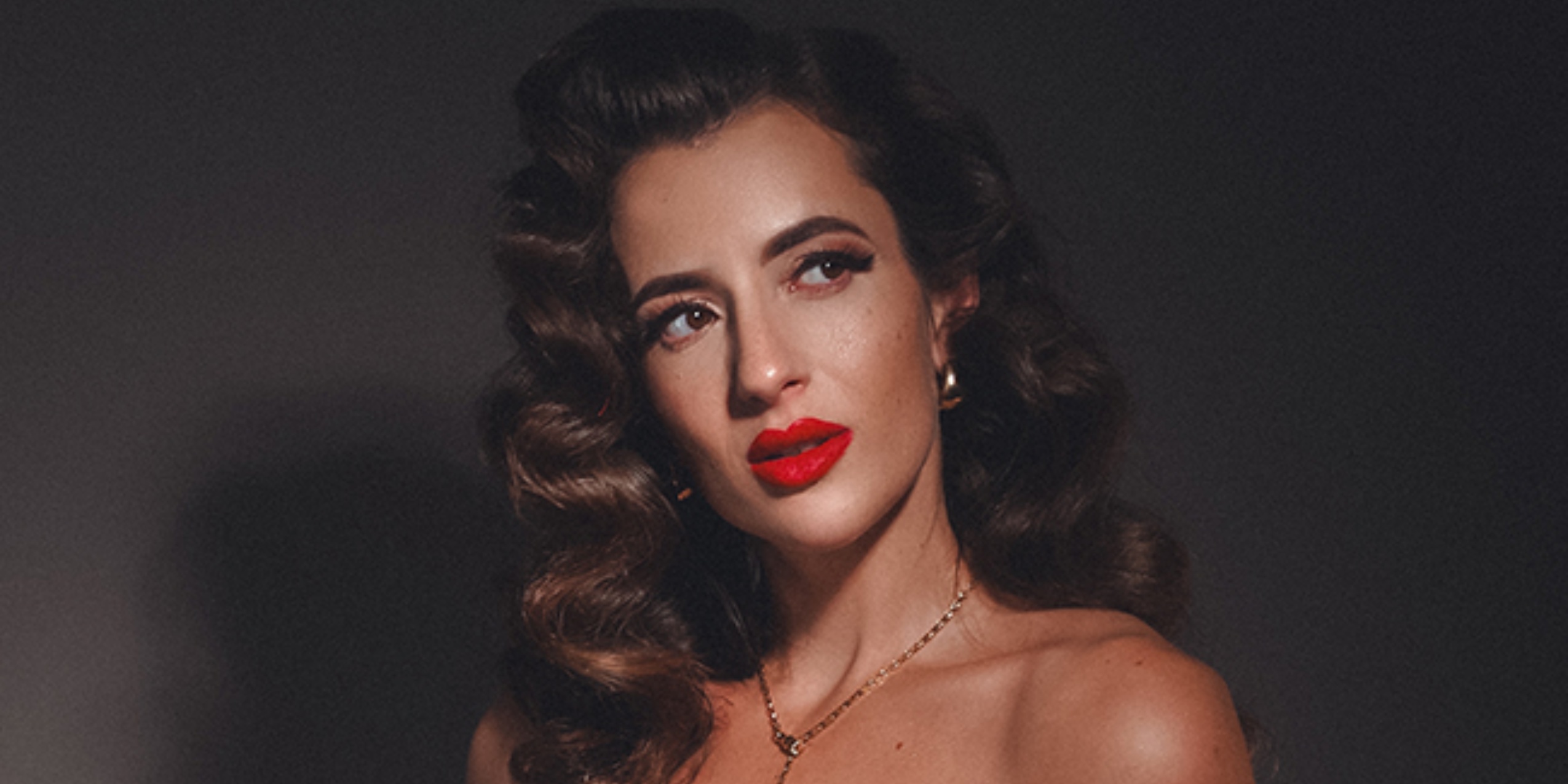 Kvinde med bølget hår og rød læbestift, foran mørkegrå baggrund.