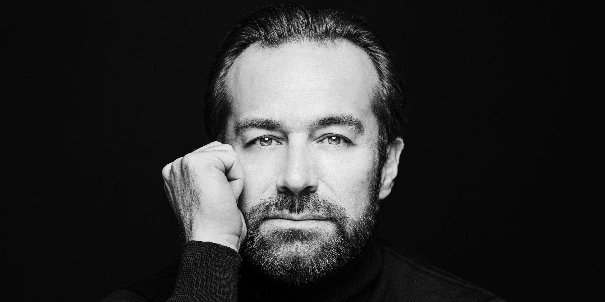 Mand hviler sit hoved ved knyttet hånd foran sort baggrund