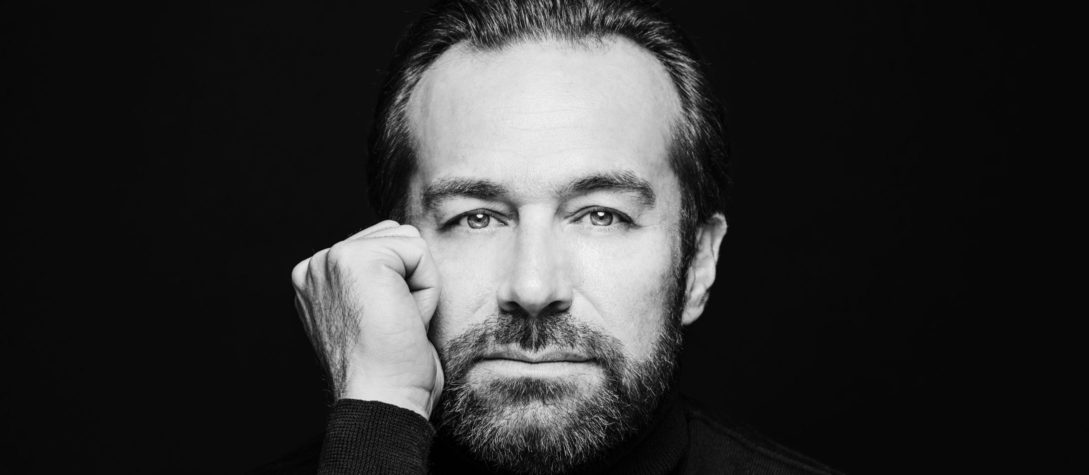 Mand hviler sit hoved ved knyttet hånd foran sort baggrund