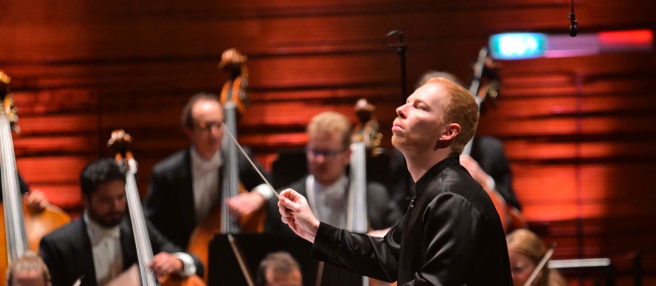 Dmitry Matvienko i profil dirigerer et stort orkester i rød sal