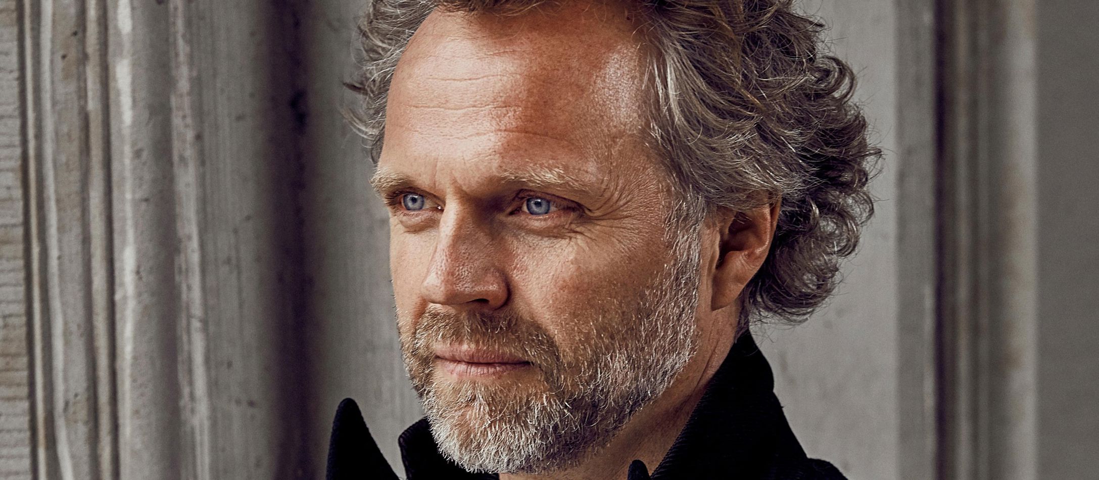 Dirigenten Thomas Søndergård i halvprofil med blå øjne kigger mod sin højre og har flot krøllet gråt hår.