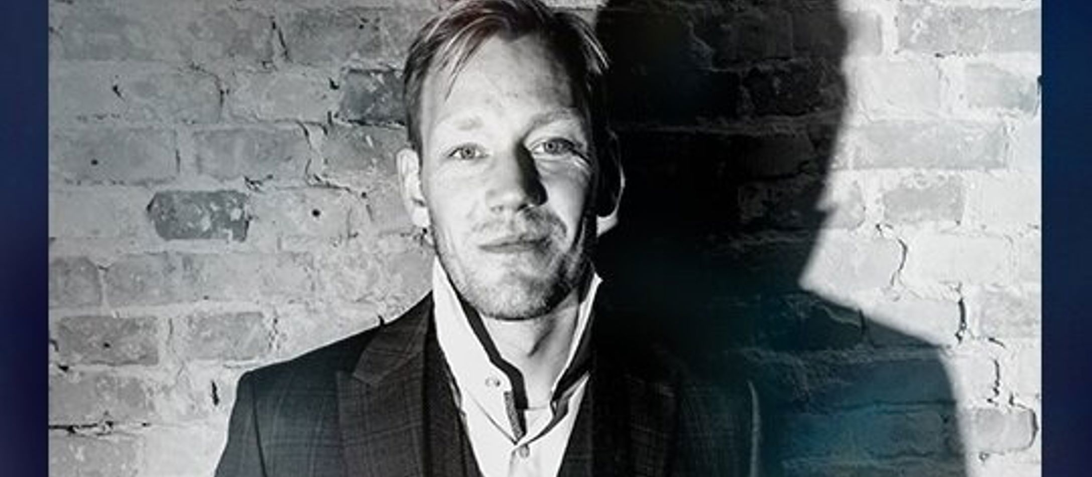 James Sherlock dirigent til Gaming X Symphony i sort/hvid foran murstensmur.