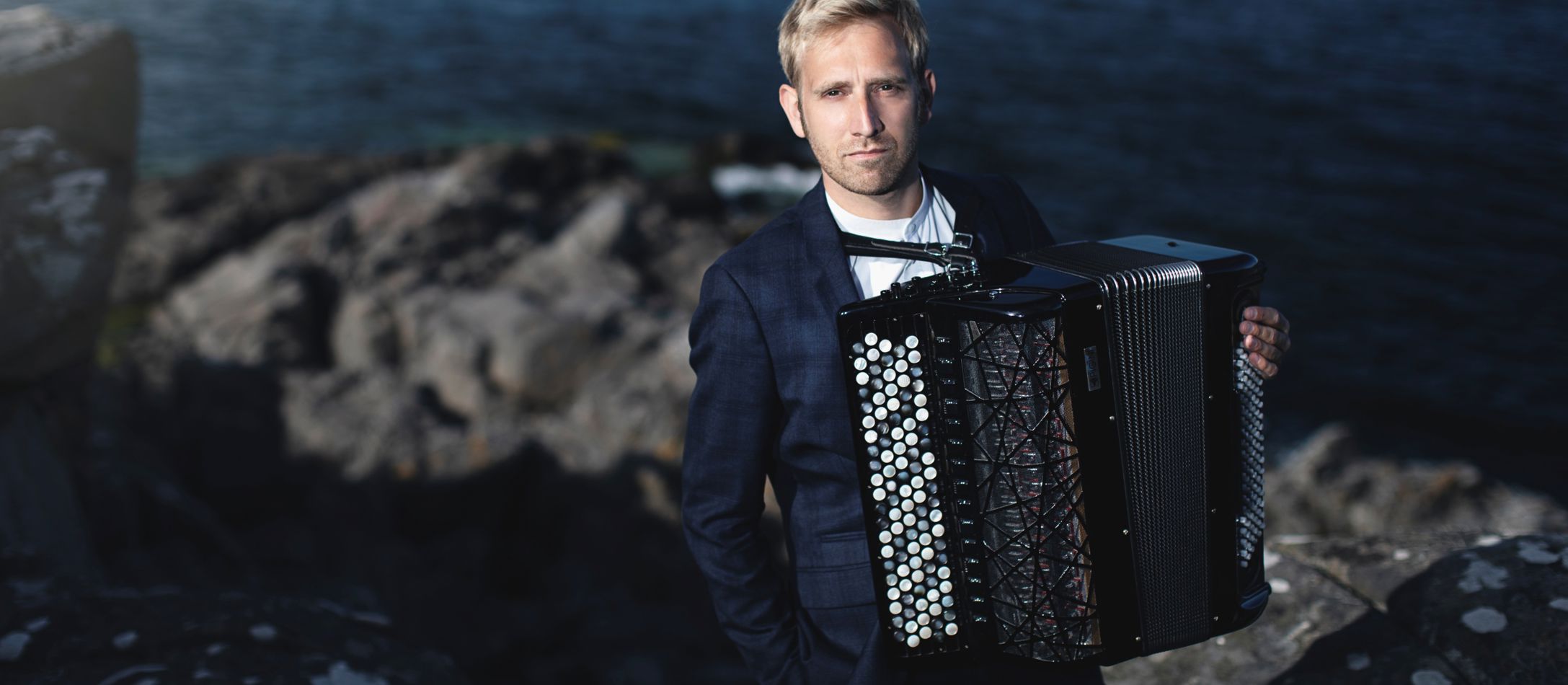 Mand med en akkordeon står på en klippeformation ved havet