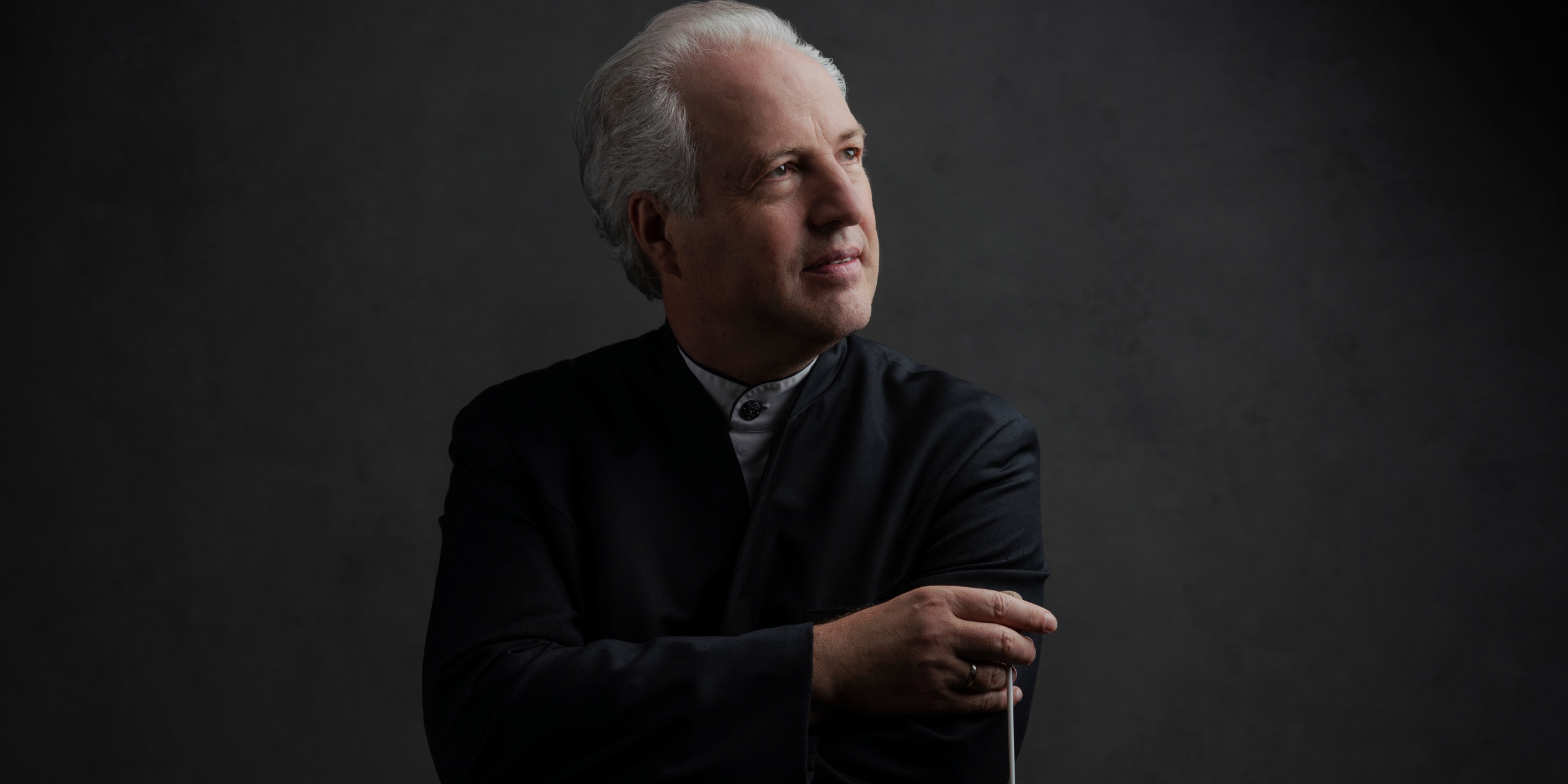 Mand i sort med en dirigentstok foran grå væg