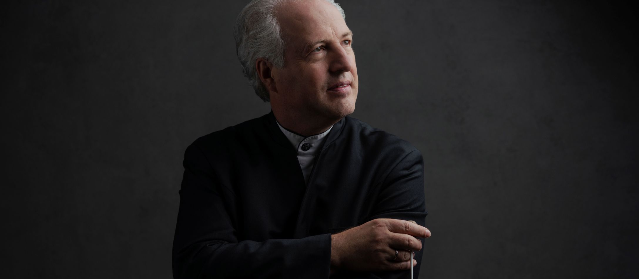 Mand i sort med en dirigentstok foran grå væg