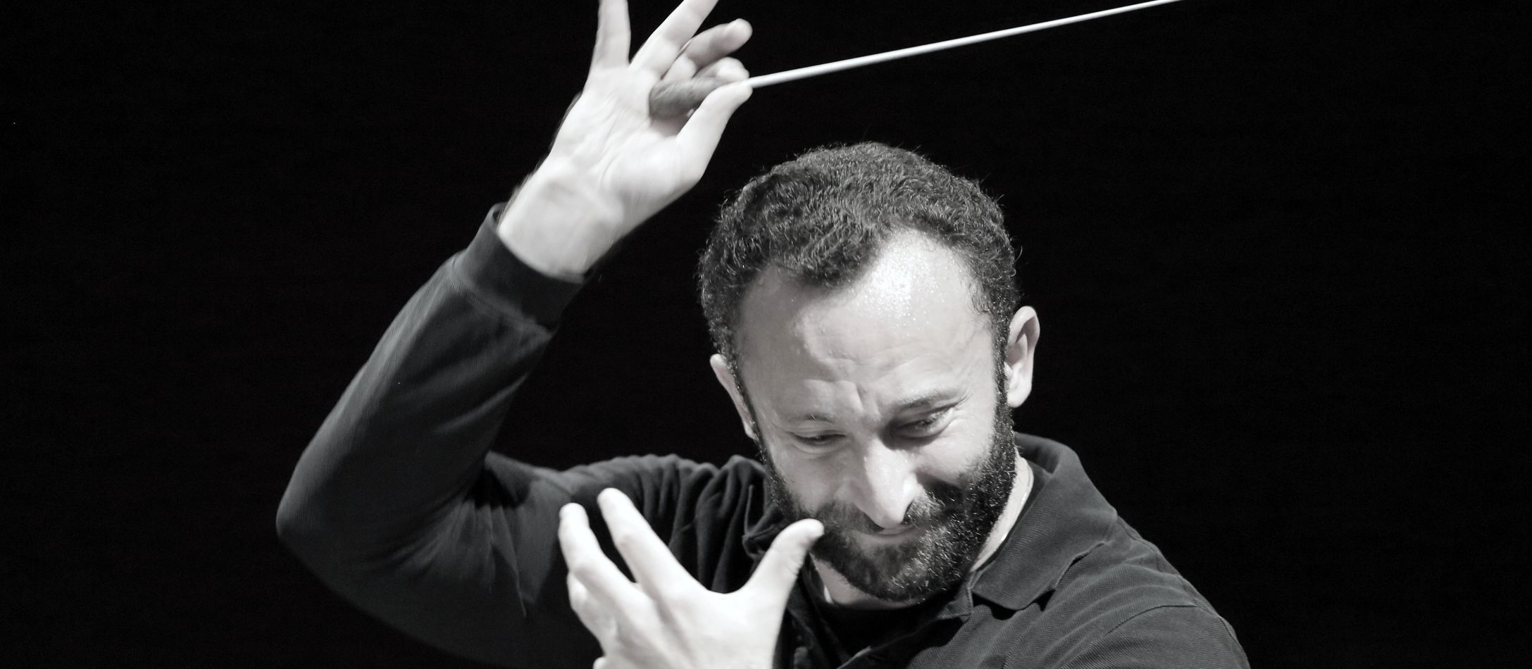 Mand med dirigentstok hævet over hovedet.