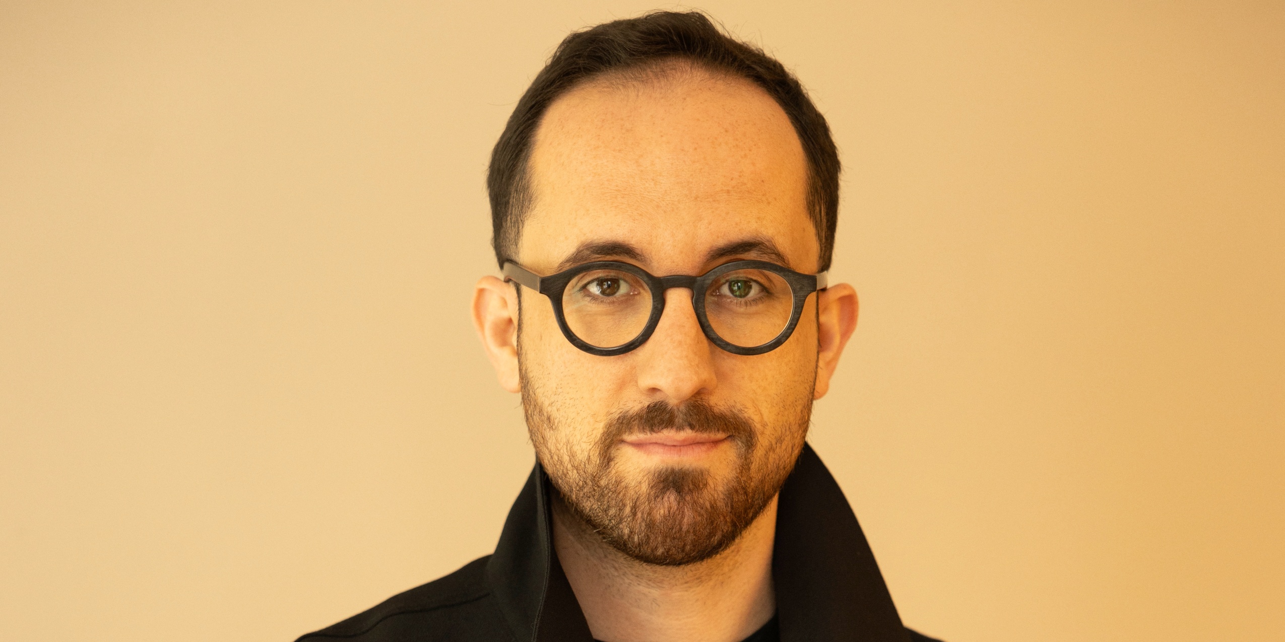 Mand med briller, kigger ind i kameraet foran en gul baggrund.