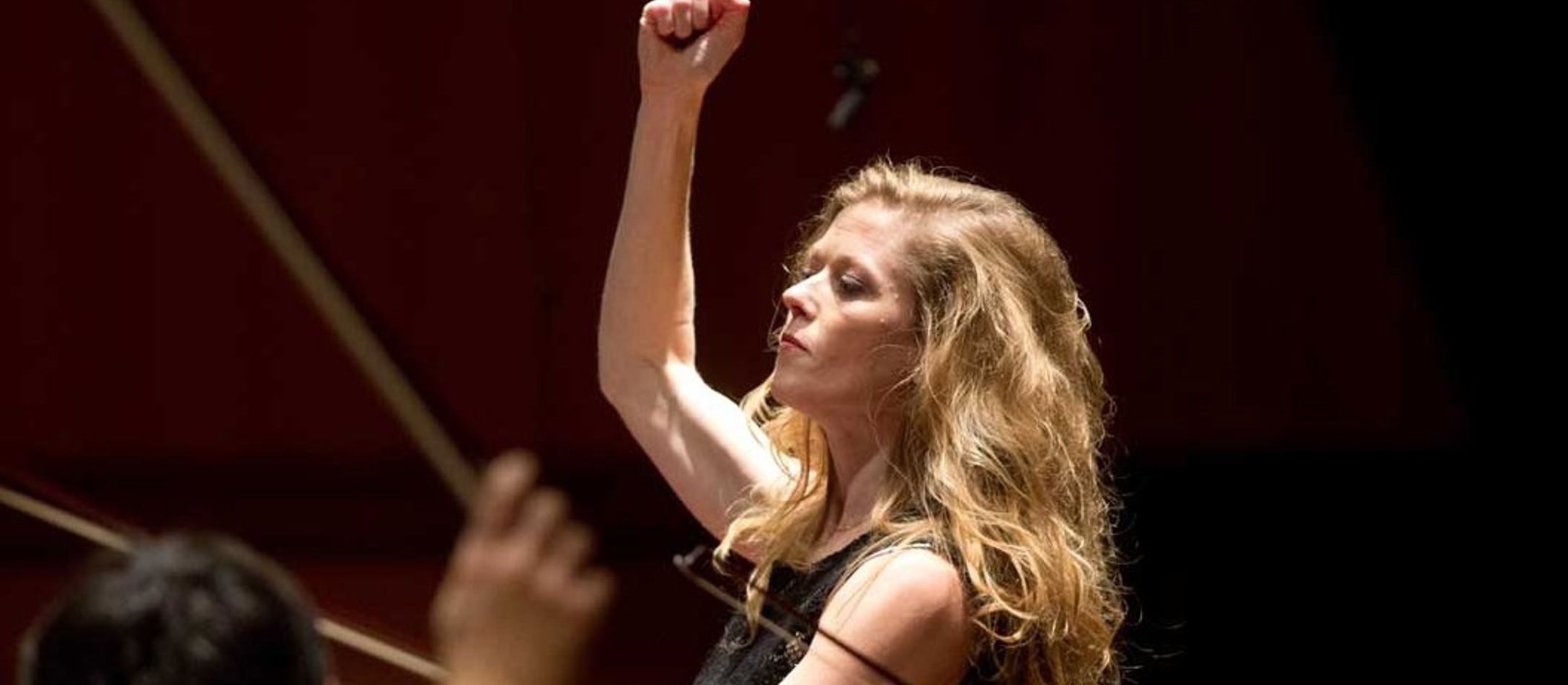 Barbara Hannigan dirigerer med en hånd i vejret og alvorligt udtryk i ansigtet fra profil.