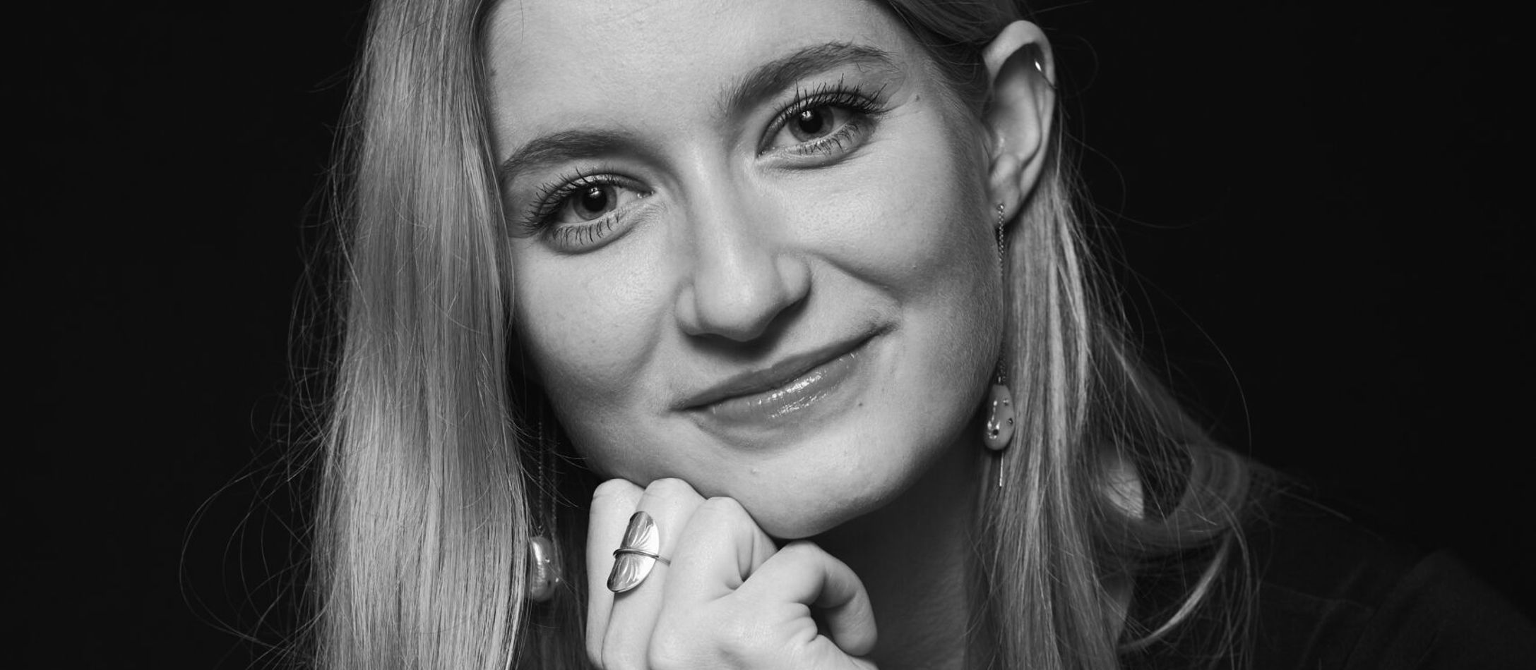 Lyshårede Louise McClelland Jacobsen i sort hvid med ansigtet hvilende på højre hånd kigger med milde øjne.