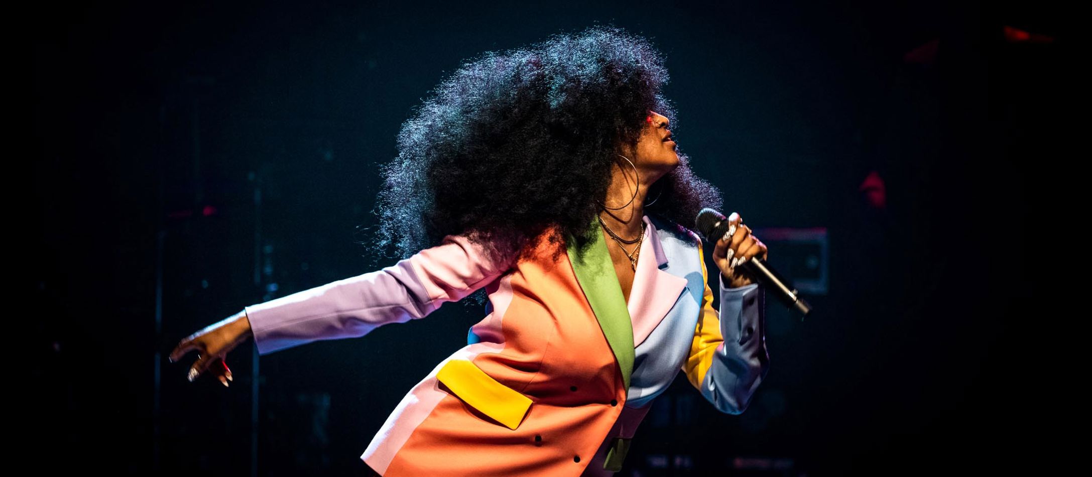 Iris Gold i profil performer i spraglet jakkesæt og stort afrohår ser tjekket ud