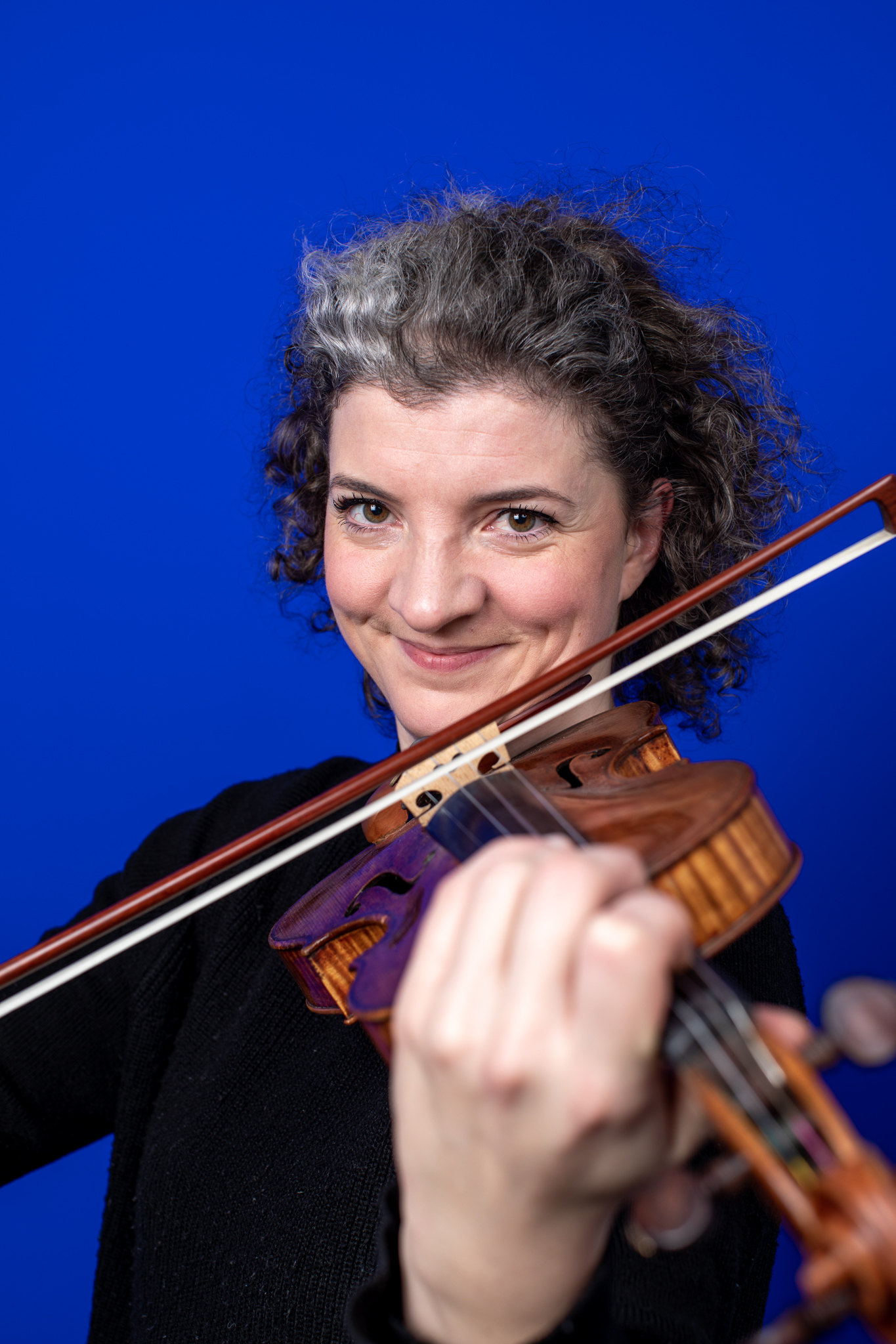 Teresa La Cour spiller smilende på sin violin på blå baggrund