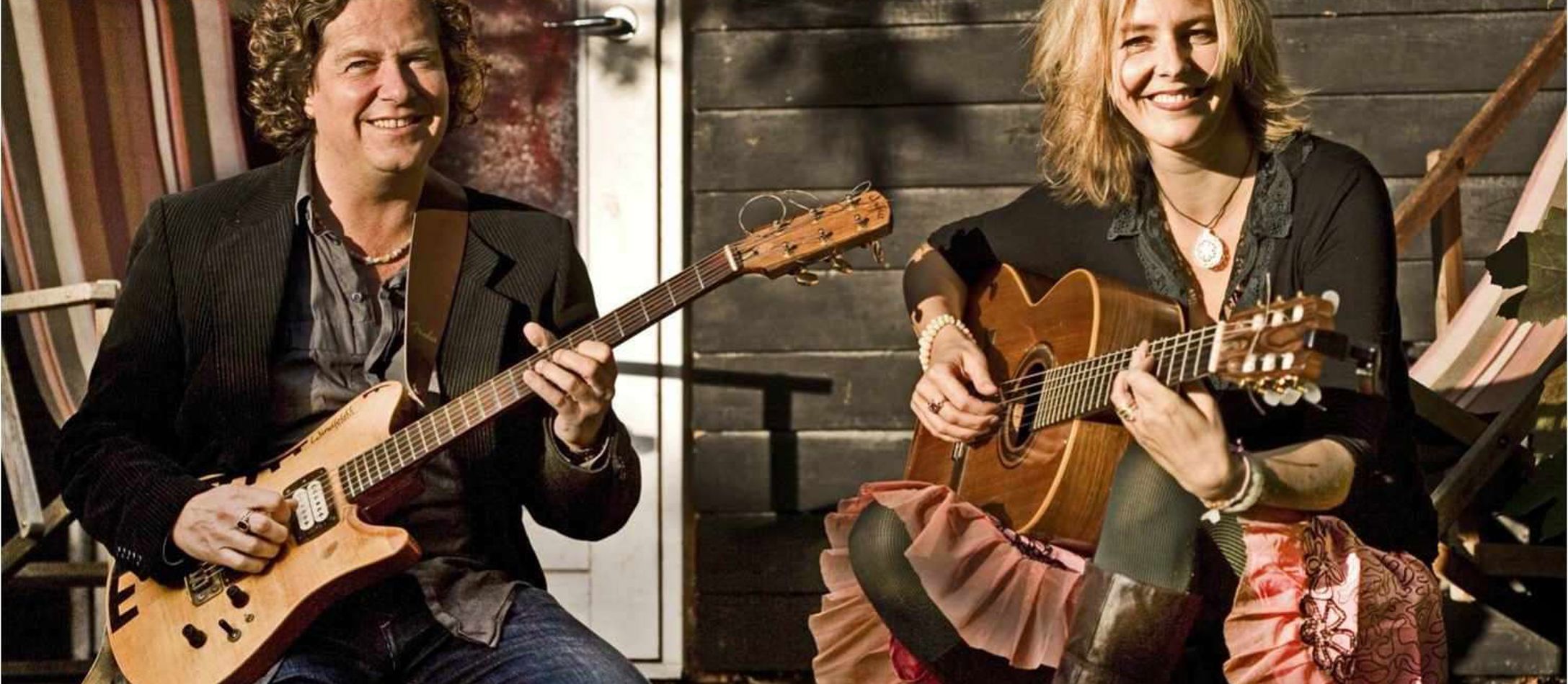 Storsmilende Sille Grønberg og Palle Windfeldt spiller guitar udendørs