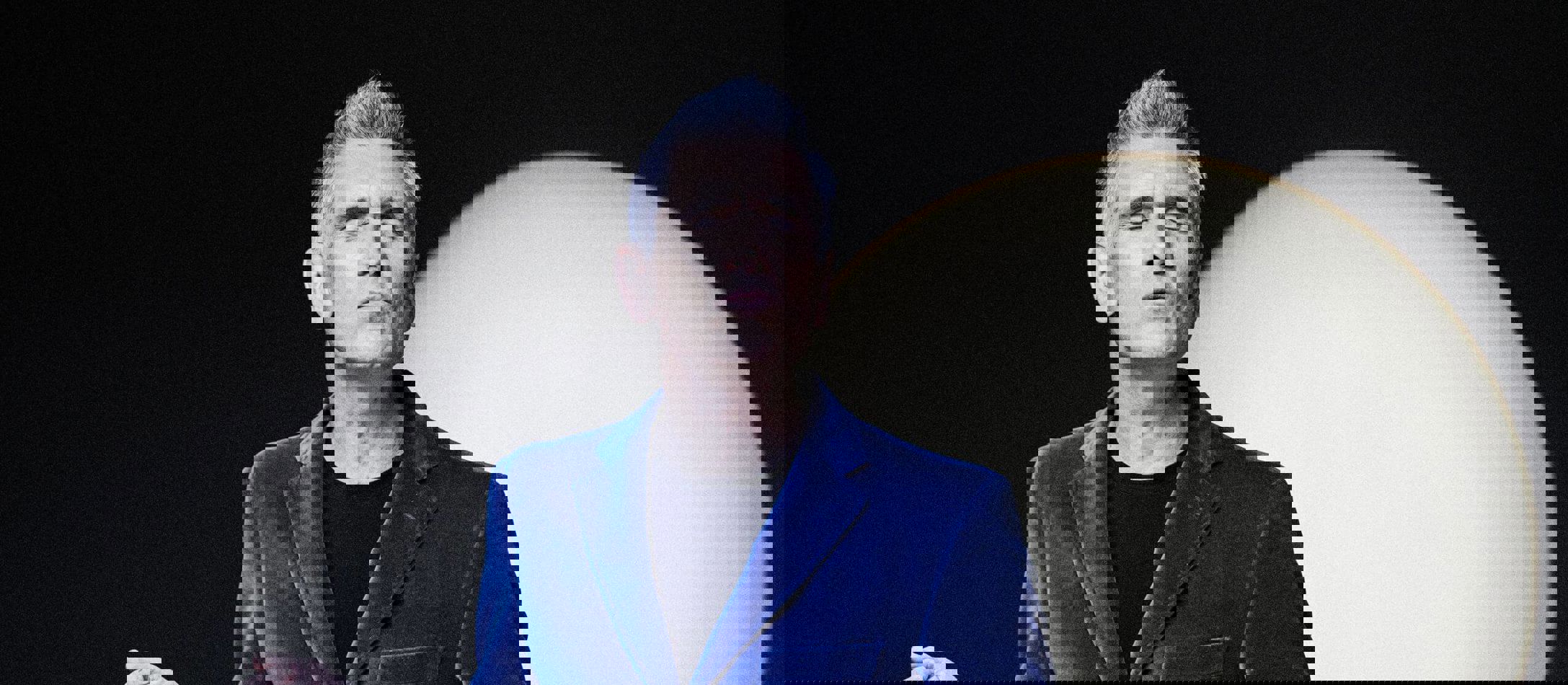 Gråhårede Curtis Stigers i blåt velour suit med lukkede øjne foran lys måne og sort baggrund