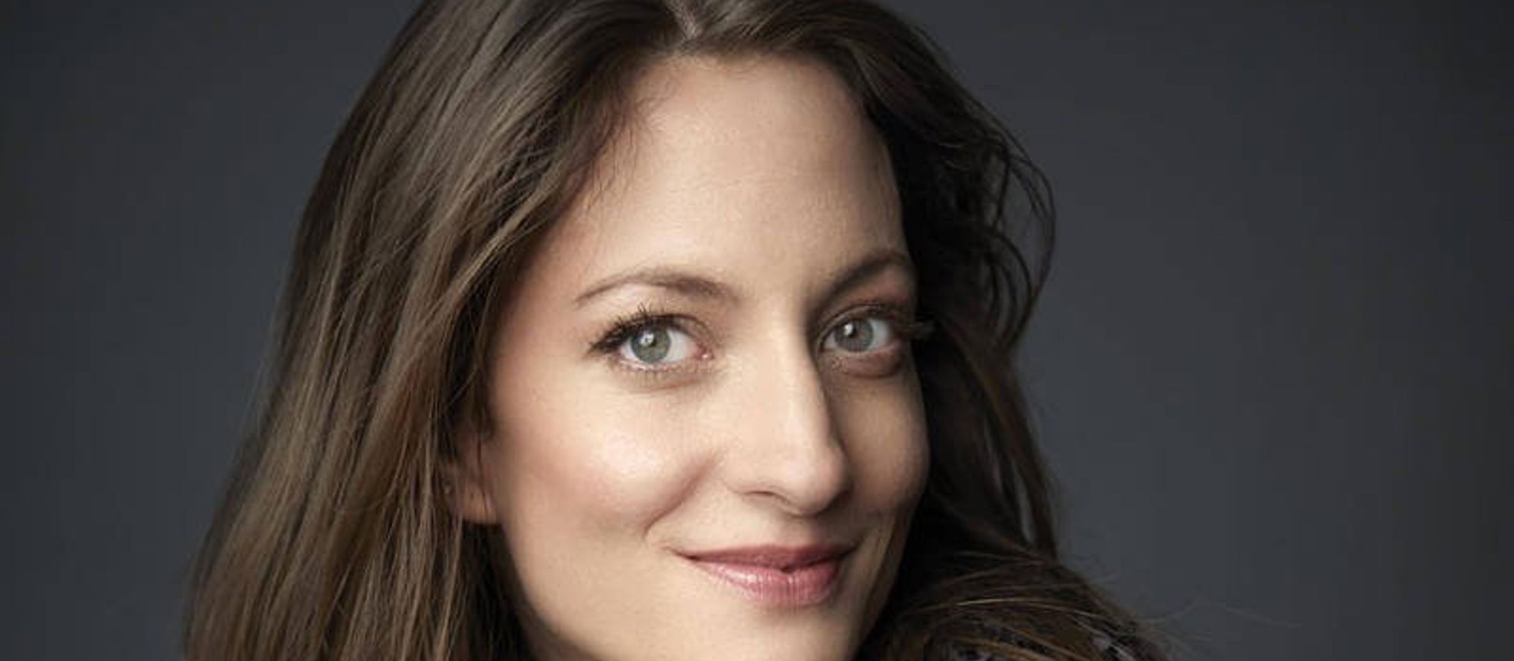 Christiane Karg med glat brunt hår smiler sødt med sine grønbrunlige øjne i blomstret sort bluse